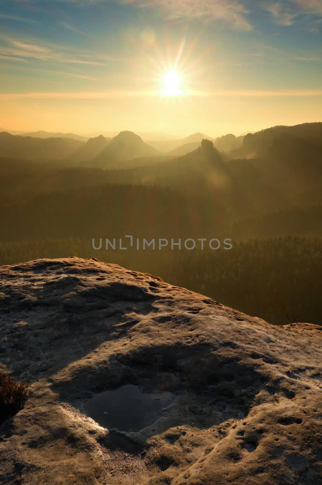 Sunrise in a beautiful mountain of Czech-Saxony Switzerland. Sandstone peaks increased from foggy background, the fog is orange due to sun rays. 