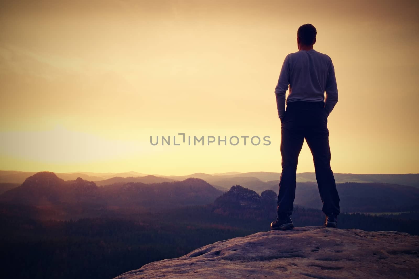 Tourist on the cliff of rock in rocky mountains park is watching over the misty and foggy morning valley to Sun