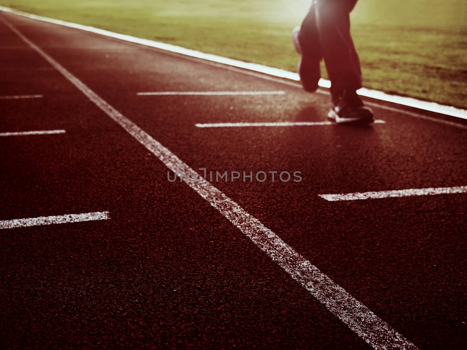 Man legs in running shoes  running on red racetrack on outdoor stadium. Sun rays and body shadow.  Sport and healthy lifestyle concept training workout