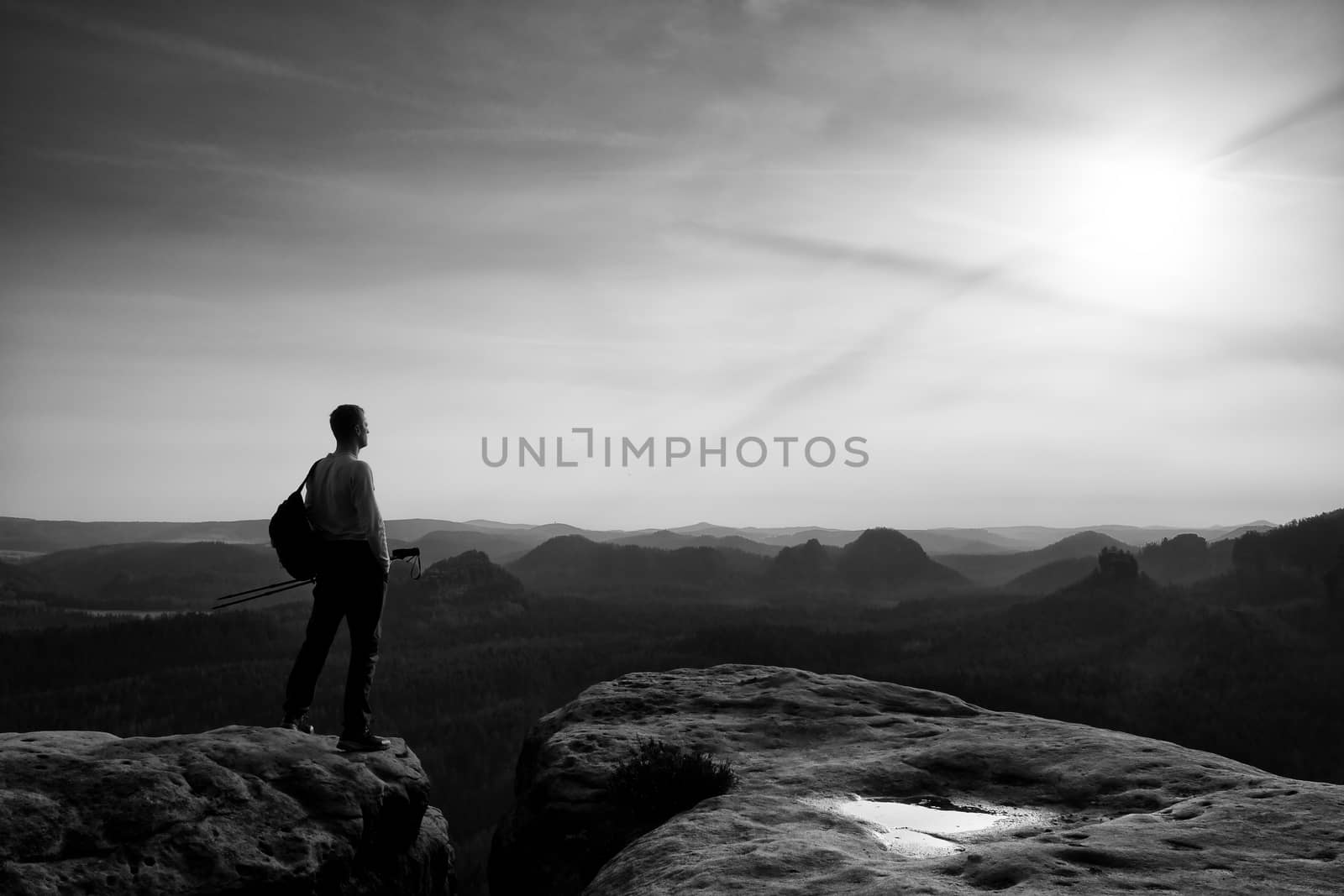 Silhouette of tourist. . Hiker with sporty backpack on rocky view point enjoying view into misty valley. Sunny spring daybreak in rocky mountains