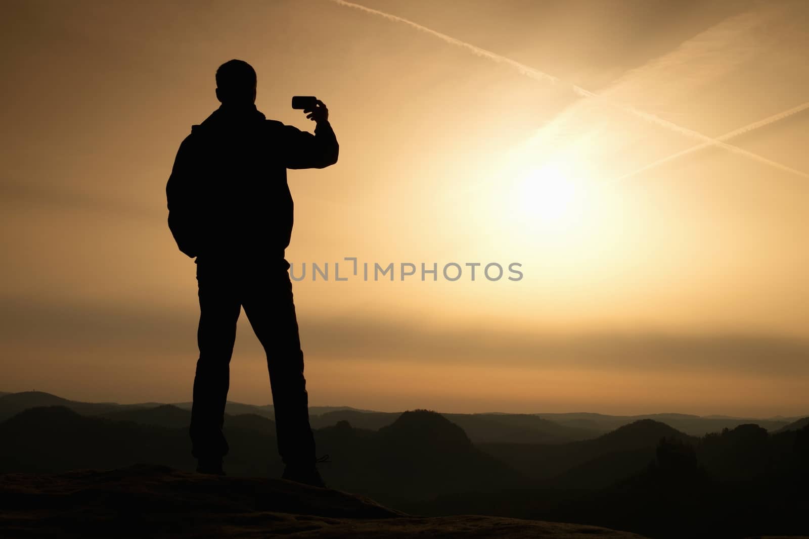Tourist hold in hand shinning phone and phototograph spring hilly landscape. Misty natuure. Phone photography on the peak of mountain at sunrise.
