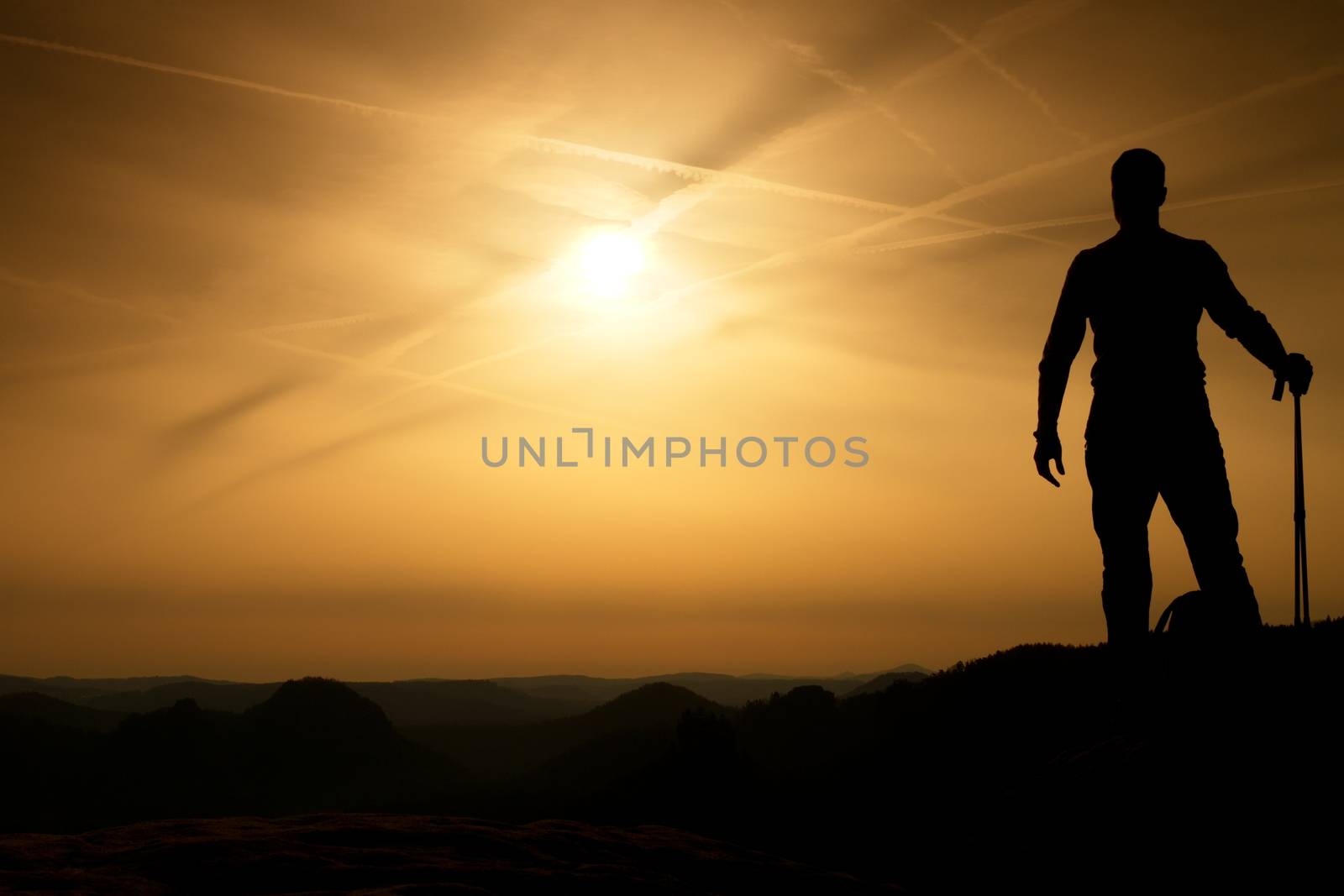 Tourist with poles in hands stand on rock watching  for next step. Sunny spring daybreak in mountains.Vignetting effect.. 