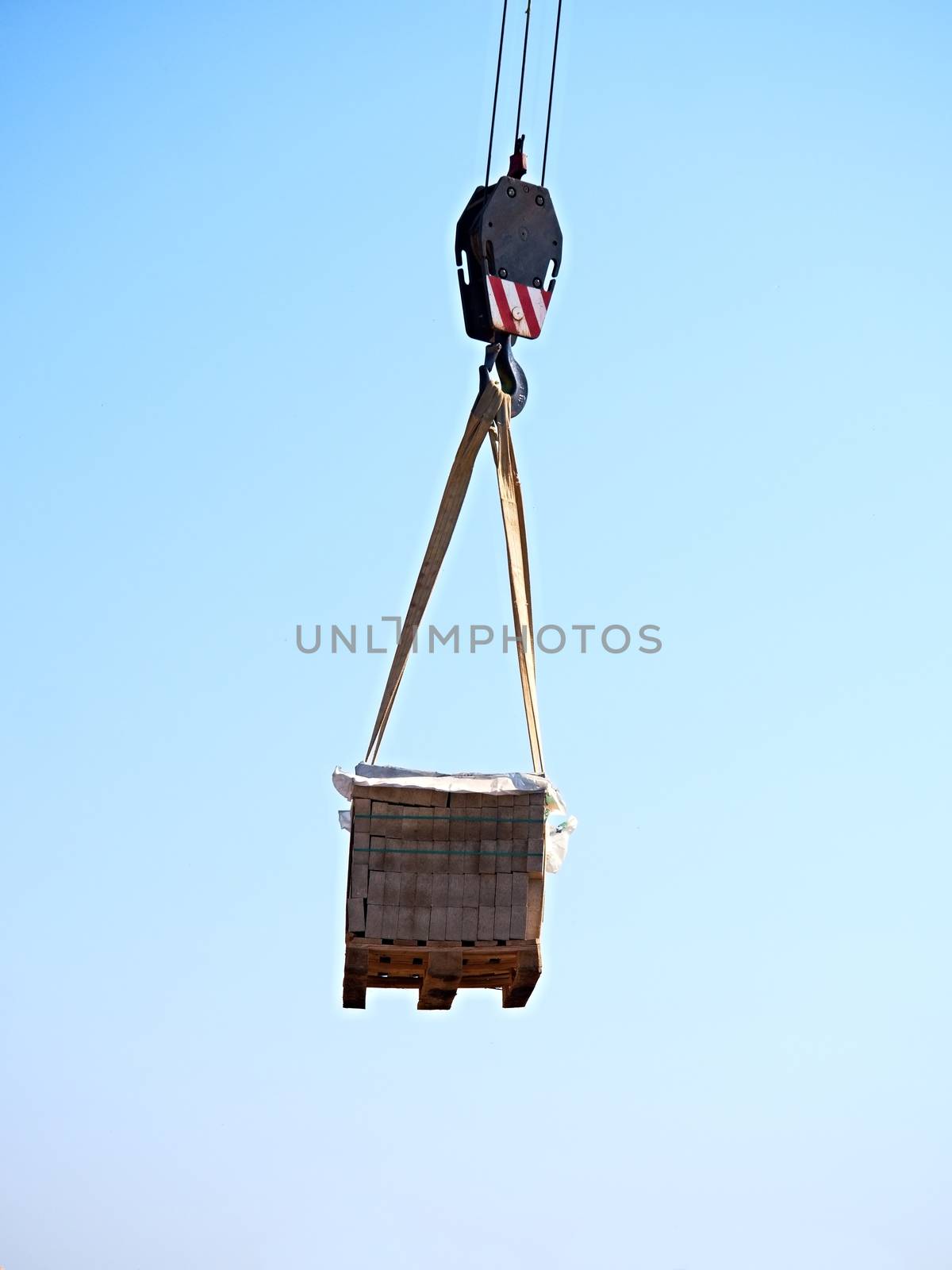 Crane Hook with Stacked white bricks on a wooden Pallet, clear blue sky in the background