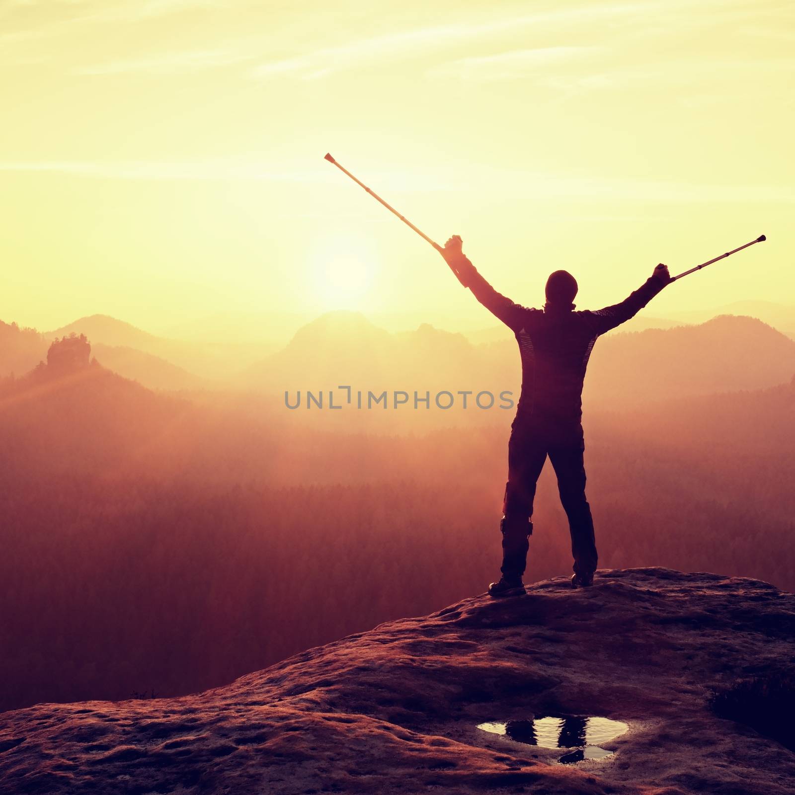 Hiker with  medicine crutch above head achieved mountain peak. Broken leg fixed in immobilizer Deep misty valley bellow silhouette of man with hand in air. Spring daybreak