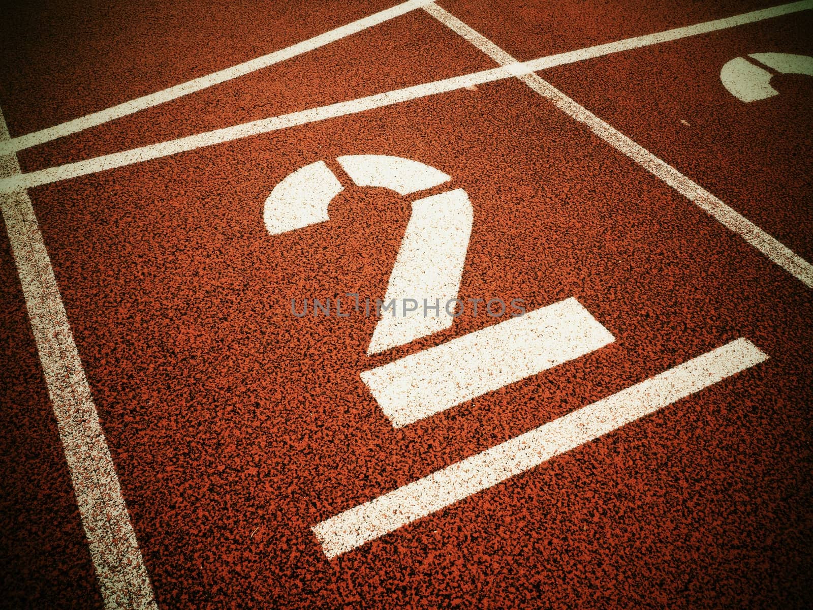 Number two. Big white track number on red rubber racetrack. Gentle textured running racetracks in small outdoor stadium.