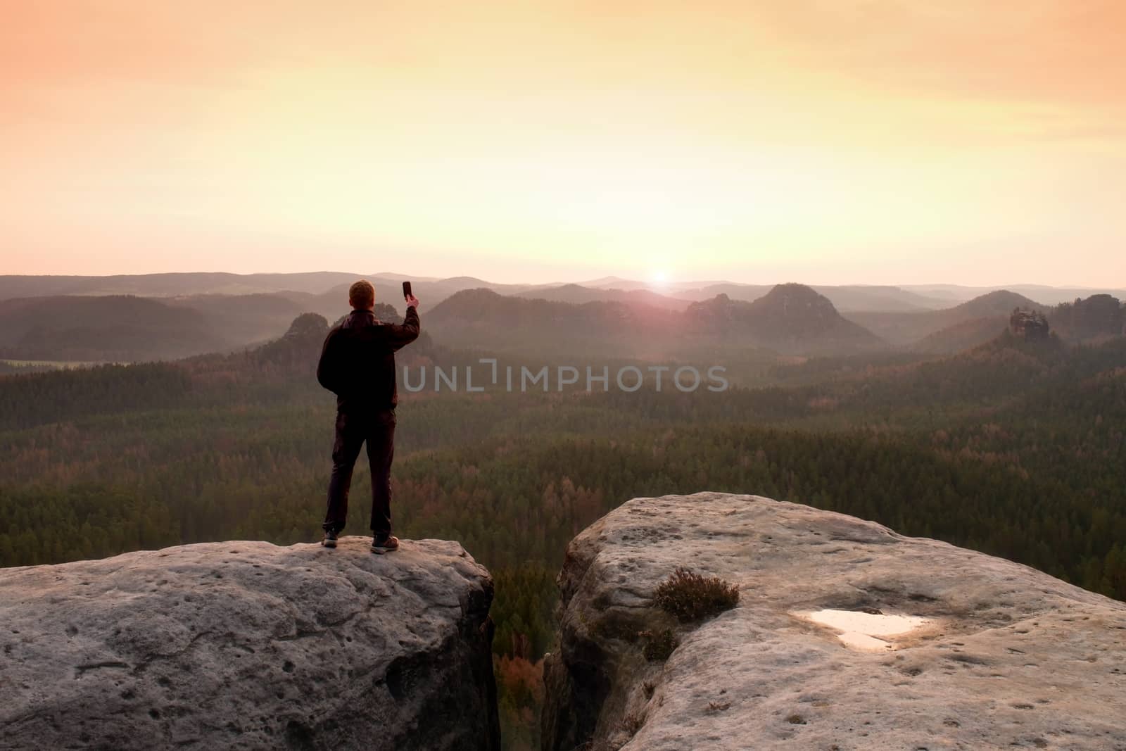 Man photography with phoneof  dreamy hilly landscape, spring orange pink misty sunrise in a beautiful valley of rocky mountains.