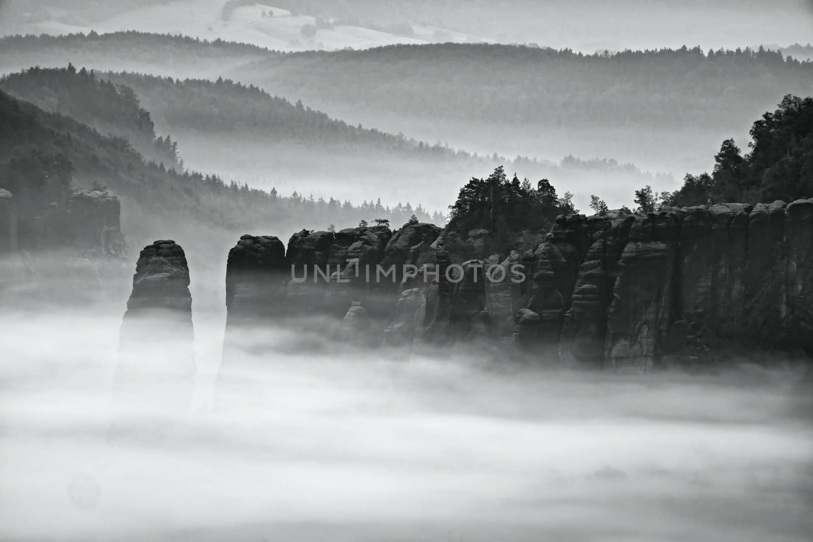 Fantastic sunrise on the top of the rocky mountain with the view into misty valley. Black and white photo