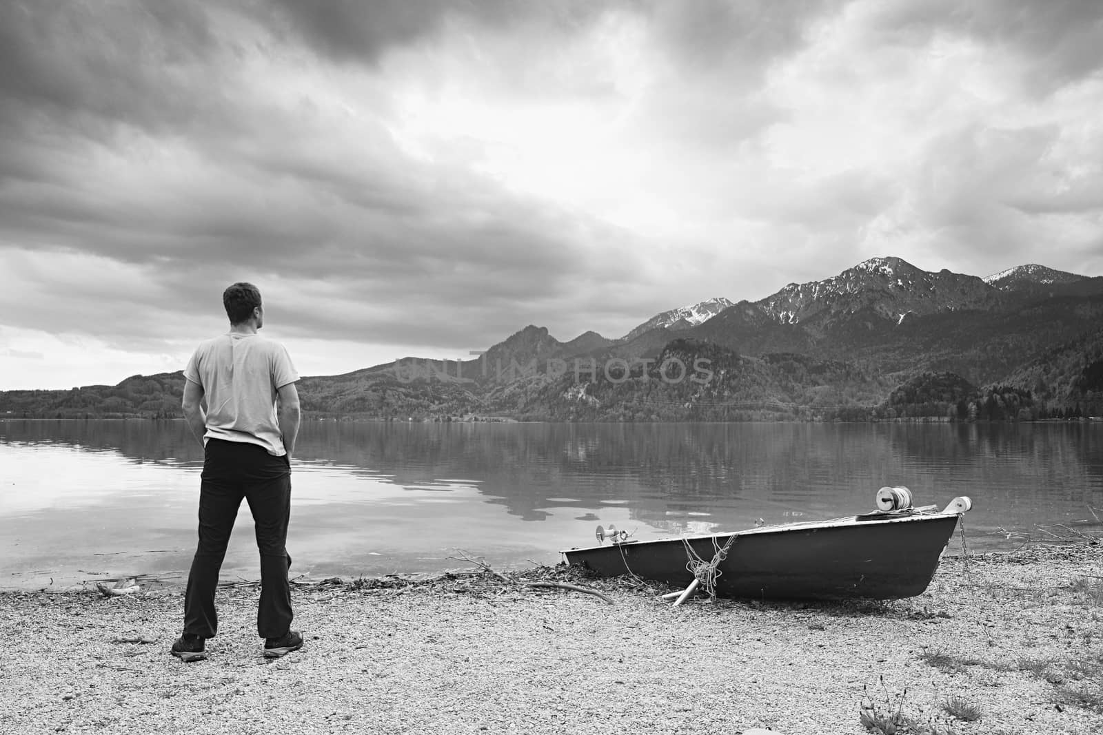 Adult man in blue shirt walk at old fishing paddle boat at mountains lake coast. Vintage photo effect by rdonar2