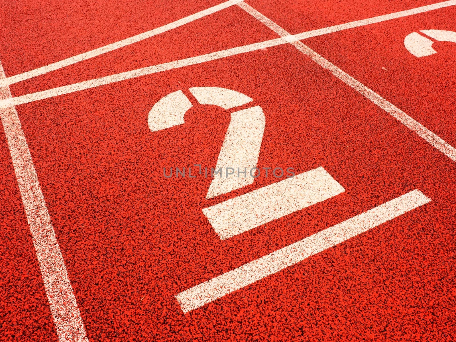 Number two. Big white track number on red rubber racetrack. Gentle textured running racetracks in small outdoor stadium.