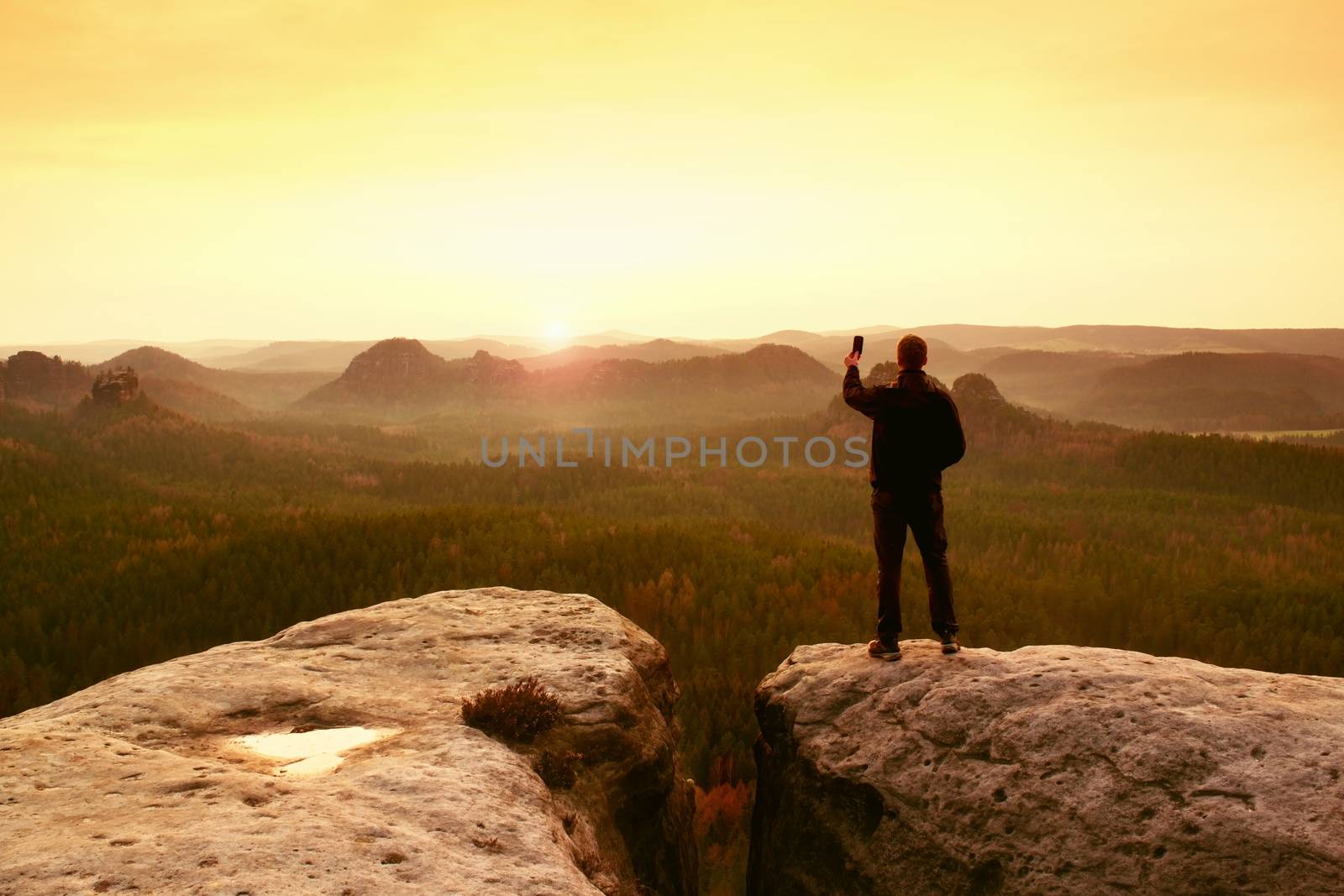 Man photography on peak of rock empire. Dreamy spring  landscape, orange pink mist