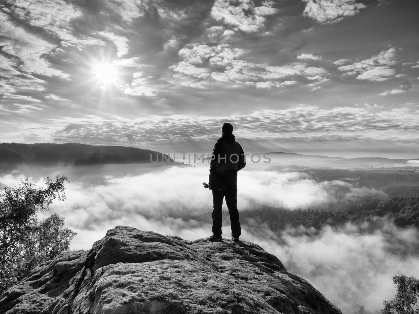 Photographer with folden tripod on end of cliff thinking. Misty landscape by rdonar2