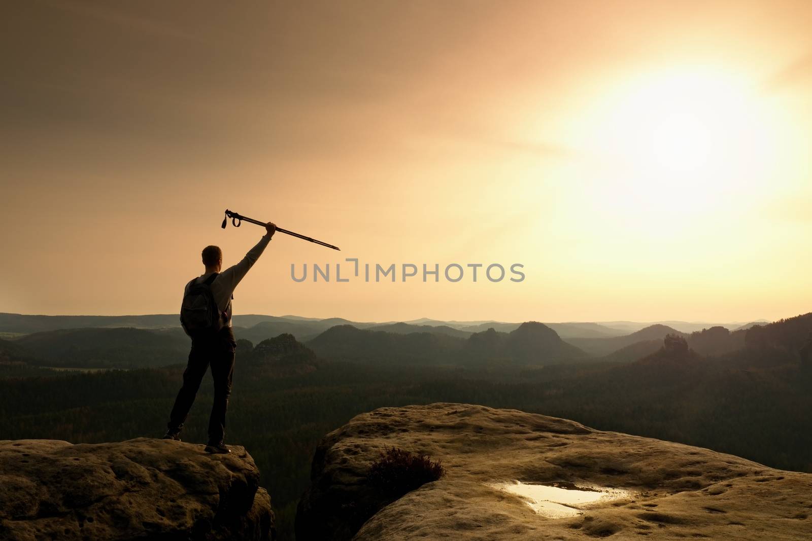 Tourist with poles in hands stand on rock watching  for next step. Sunny spring by rdonar2