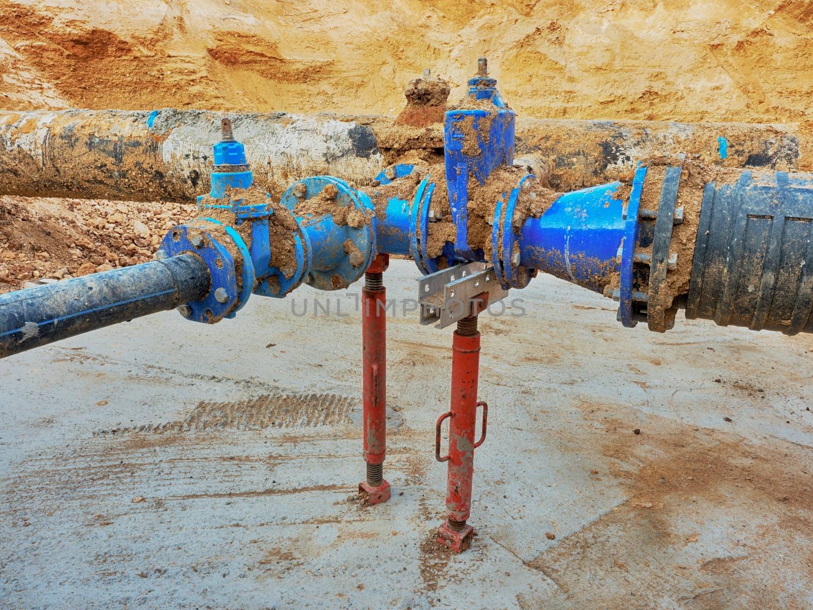 Old big drink water pipes joined with new blue gate valves and reduction joint members. Finished repaired piping waiting for covering by clay. Extreme kind of corrosion, metal corroded texture.