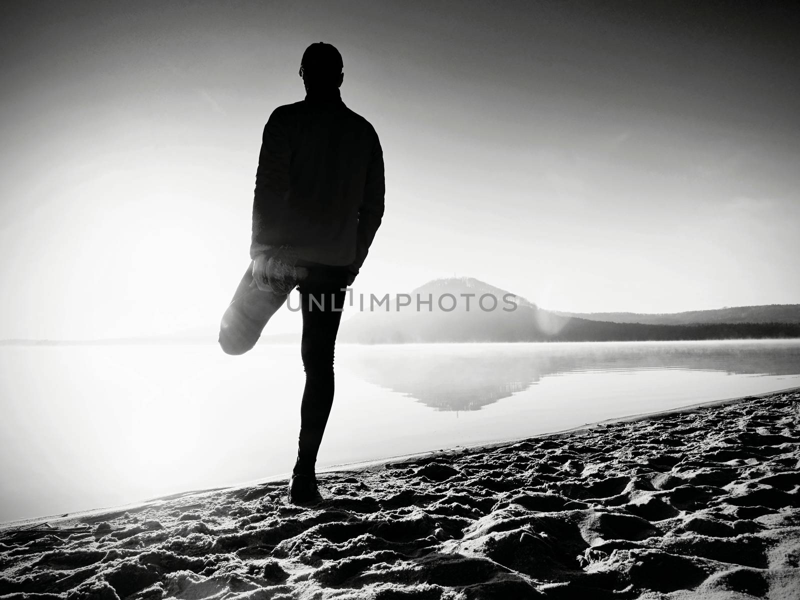Man exercising on beach.  Silhouette of active man exercising  and stretching at lake by rdonar2