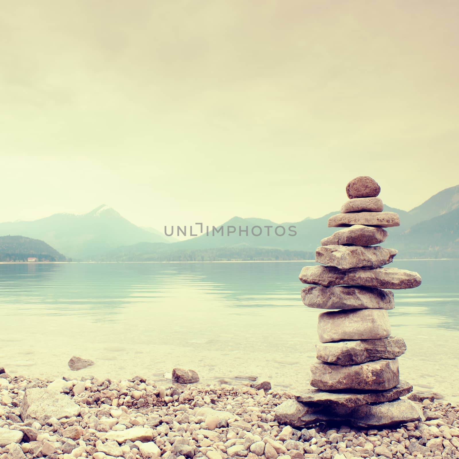 Balanced stone pyramide for memory. Stony shore of blue water of mountain lake with level mirror. Children built pyramid from pebbles.  Poor lighting conditions.