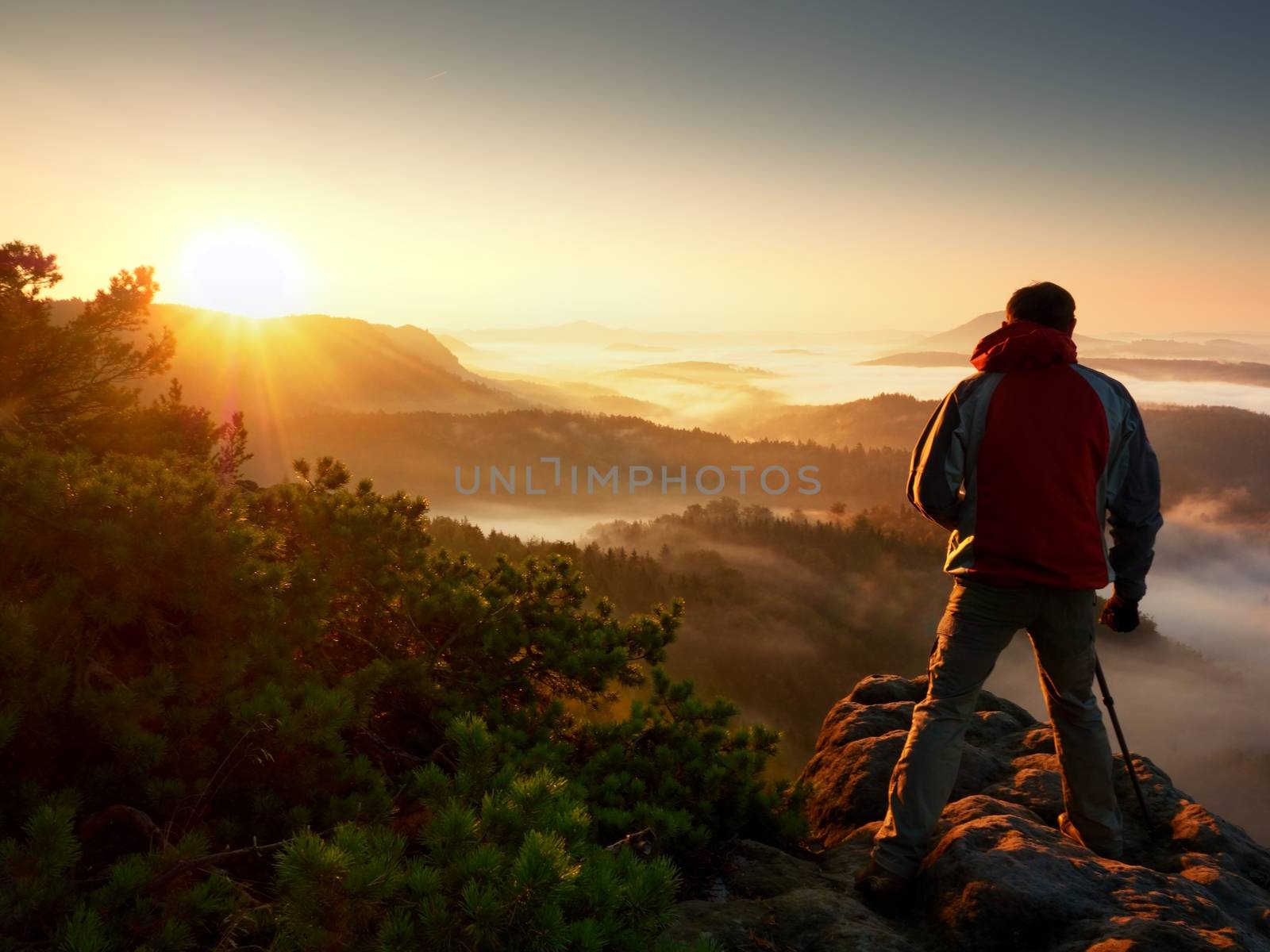 Happy photo enthusiast  enjoy  photography of  fall daybreak in nature on cliff on rock. Dreamy fogy landscape, misty sunrise in a beautiful valley below