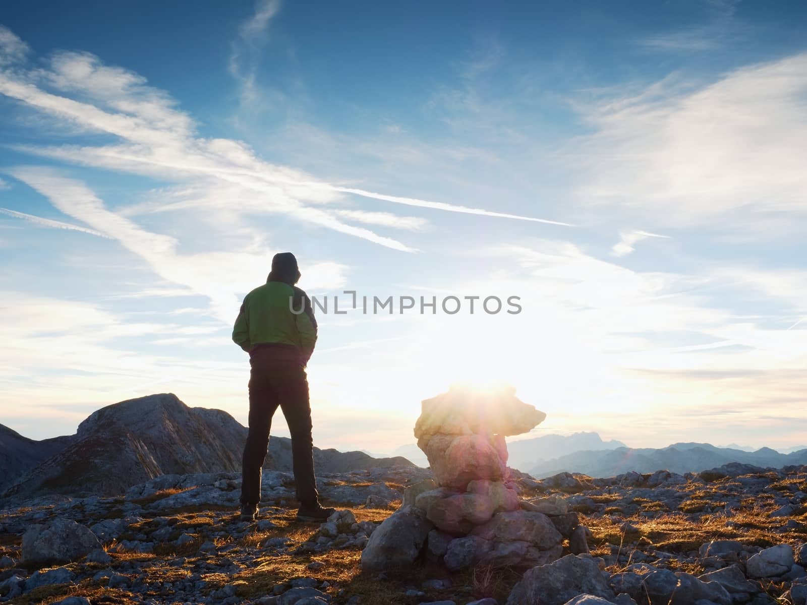 Tourist in green outdoor jacket on rocky view point. Stacked broken stones in pyramid. National park Alps park at Austria Germany border.  Sunny autumnal morning.