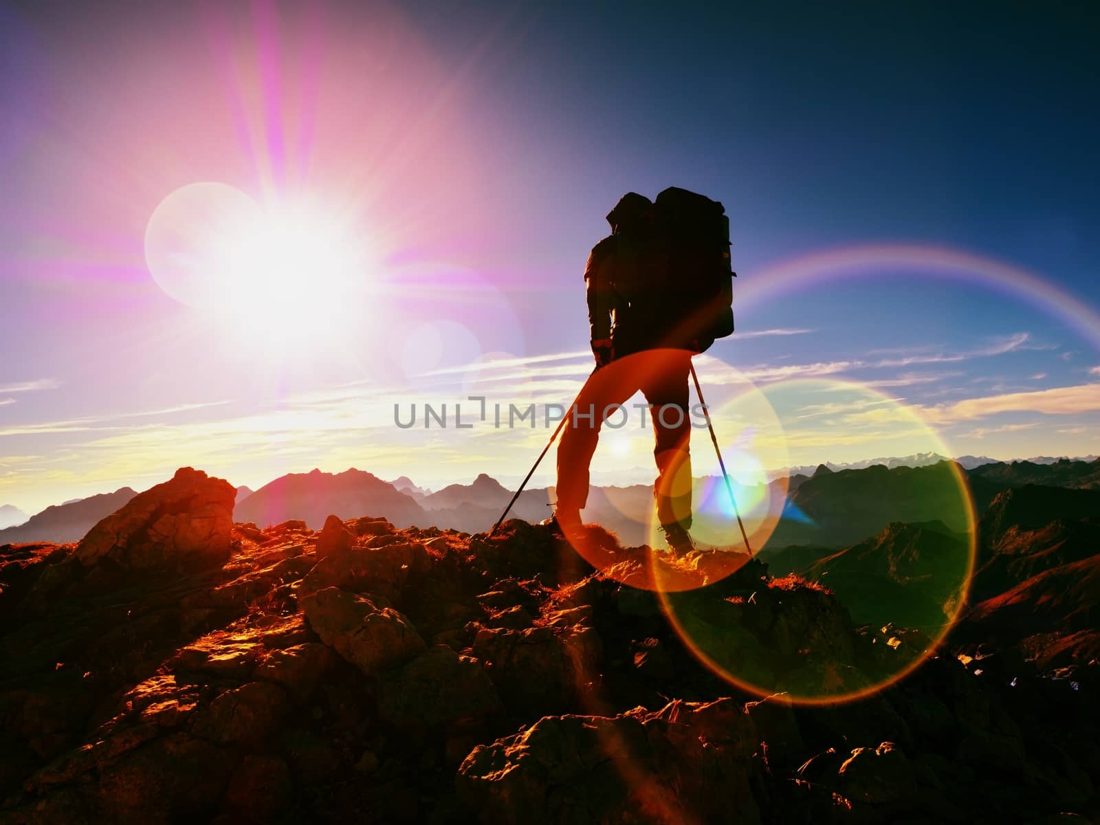 Lens flare light, strong defect. Man hiker with rucksack walk  on rocky peak. Tourist  walking over rocky summit to Sun. Beautiful moment the miracle of nature.