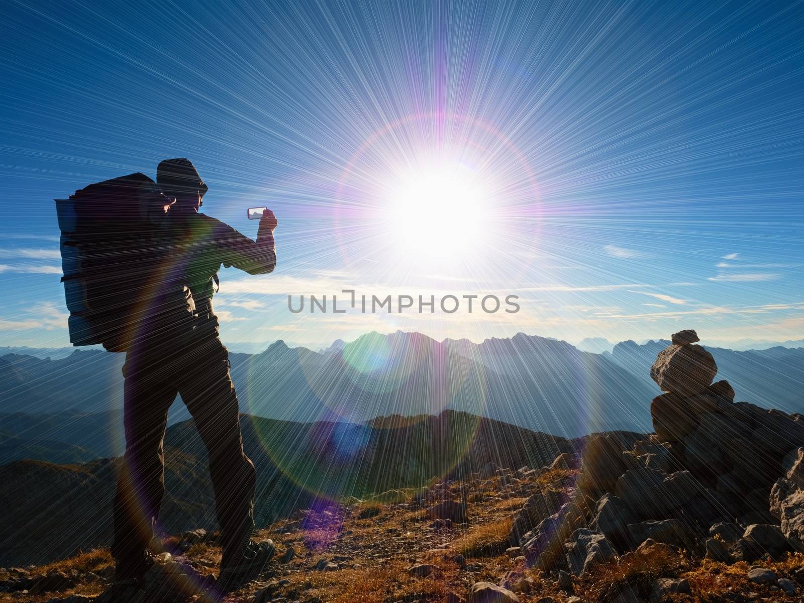 Lens flare light, strong defect. Tourist guide on Alps peak takes photo. Strong hiker with big backpack  Alpine mountain. Alone man on few days trek