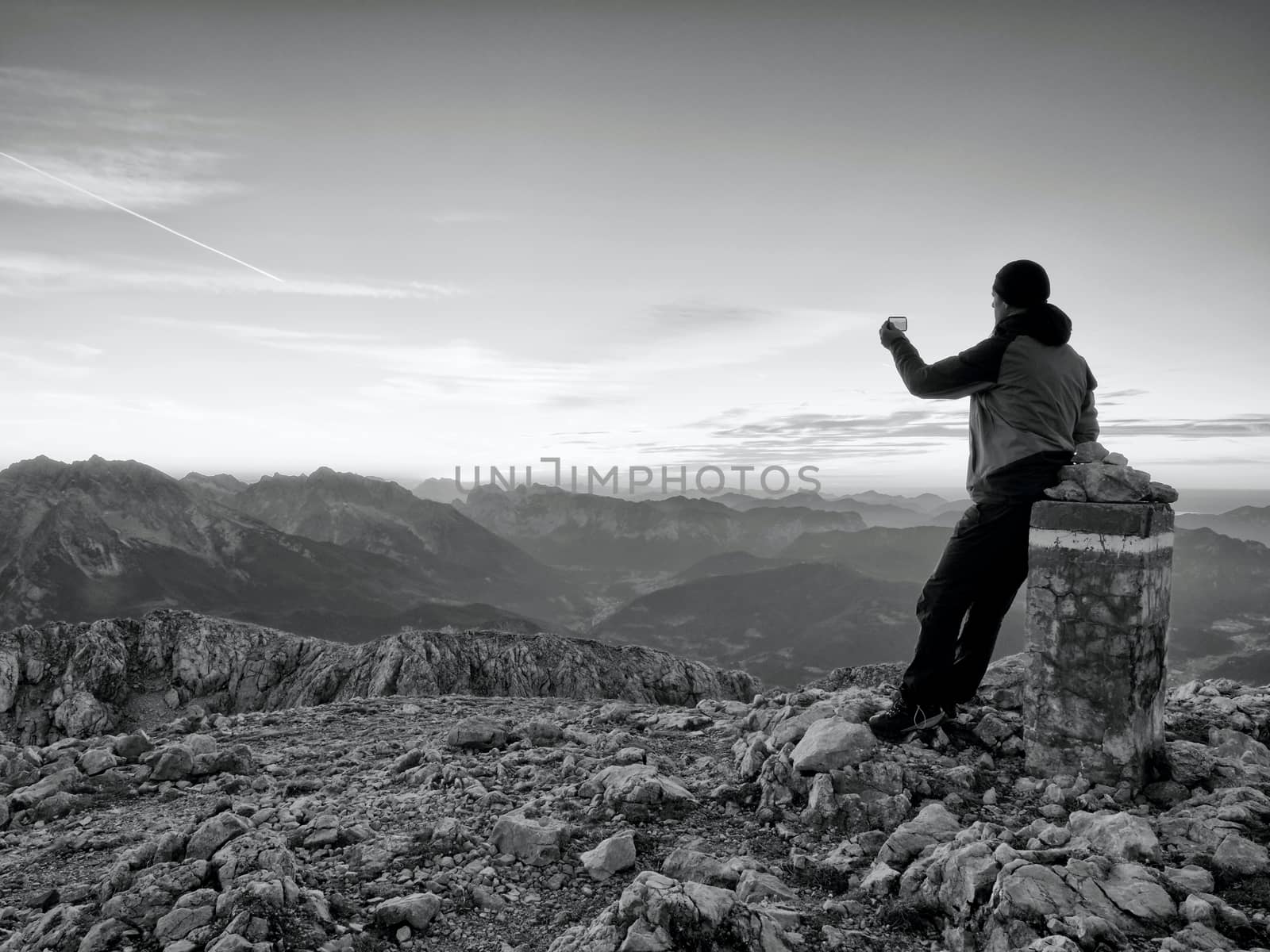 Hiker takes selfie photo. Man  sit on Austria Germany border stone on Alpine mountain. by rdonar2