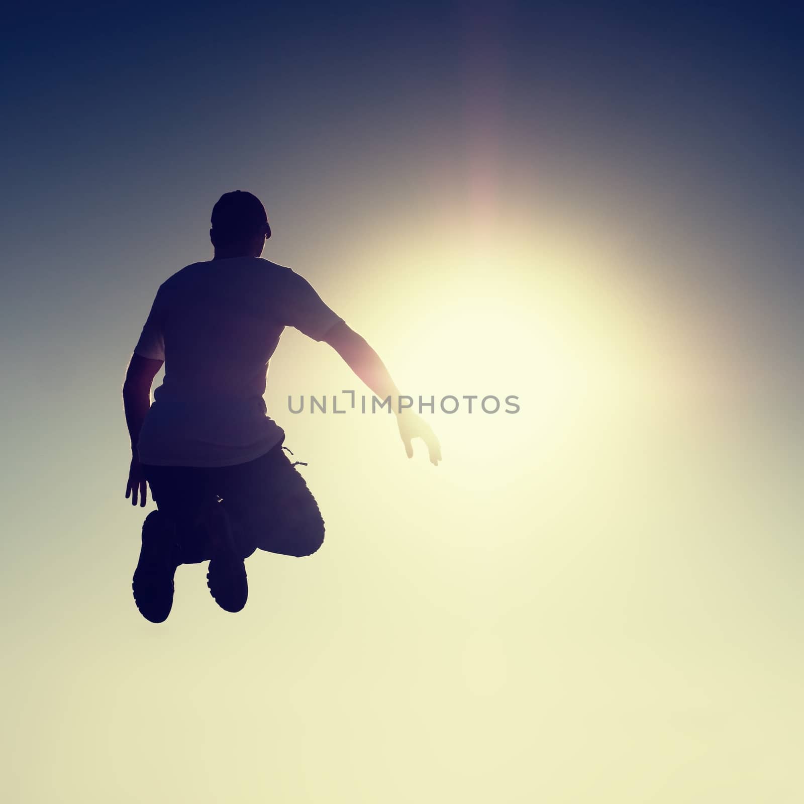 Crazy man is flying over Sun on blue sky background. Silhouette of jumping man and beautiful sunset sky. Element of design. Vintage effect.