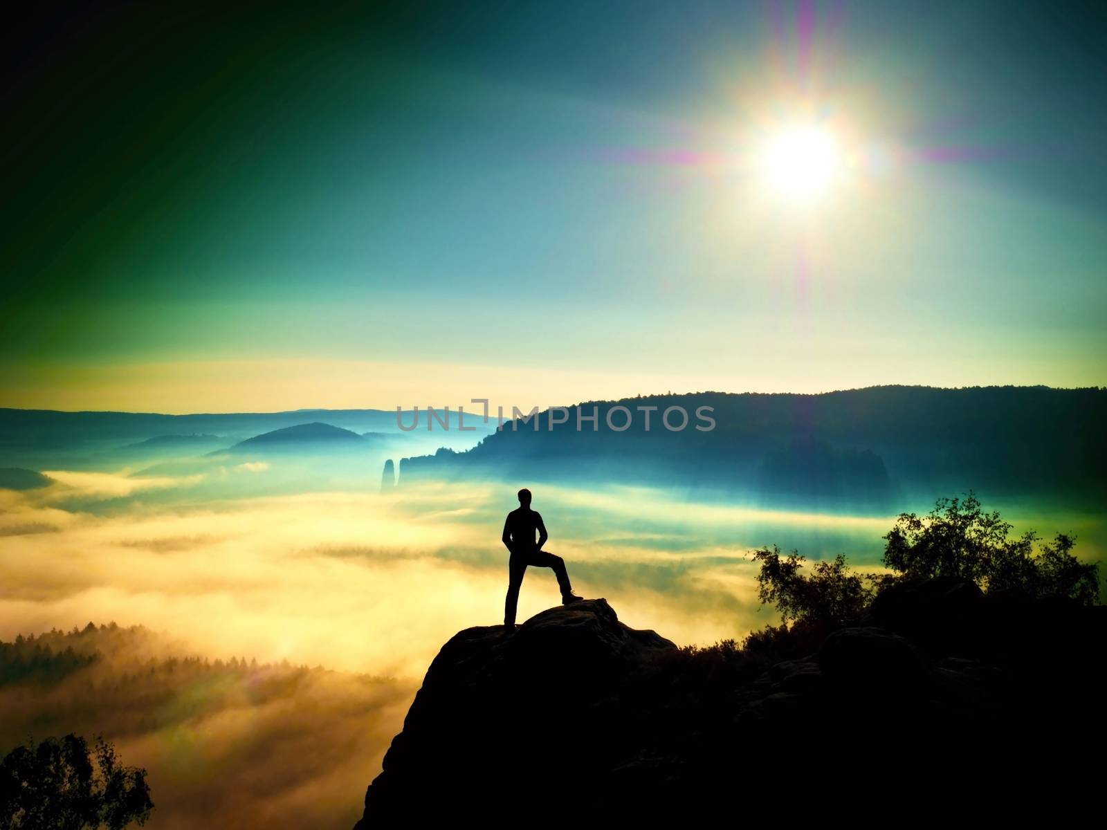 Man silhouette on the sharp peak. Satisfy hiker enjoy view. Tall man on the peak of cliff watching down to landscape. Vivid and strong vignetting effect.