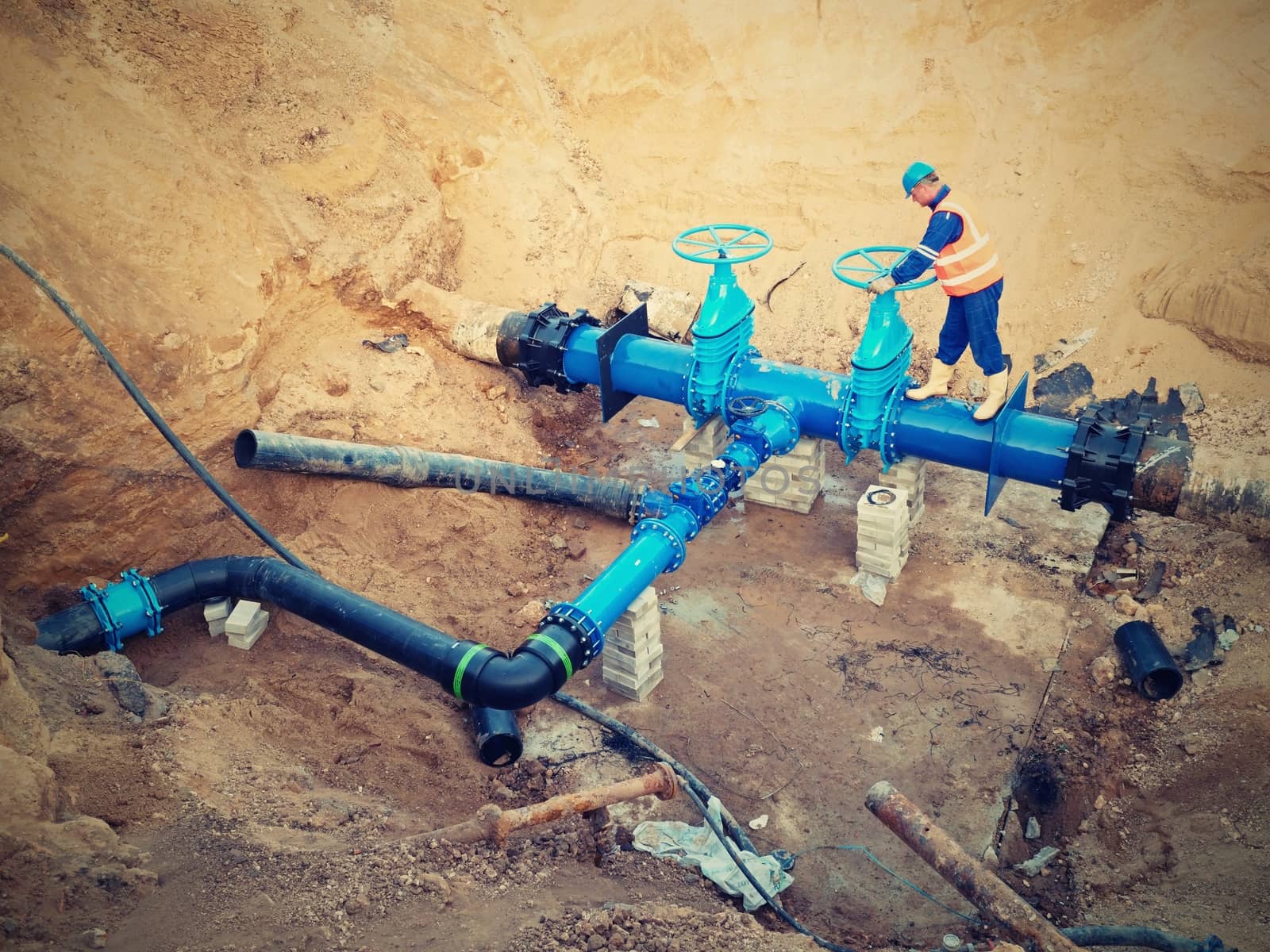 Worker works underground for reconstrucion of drink water system. Technical expert at  gate valve on new pipeline system check of repaired connection before covering by clay