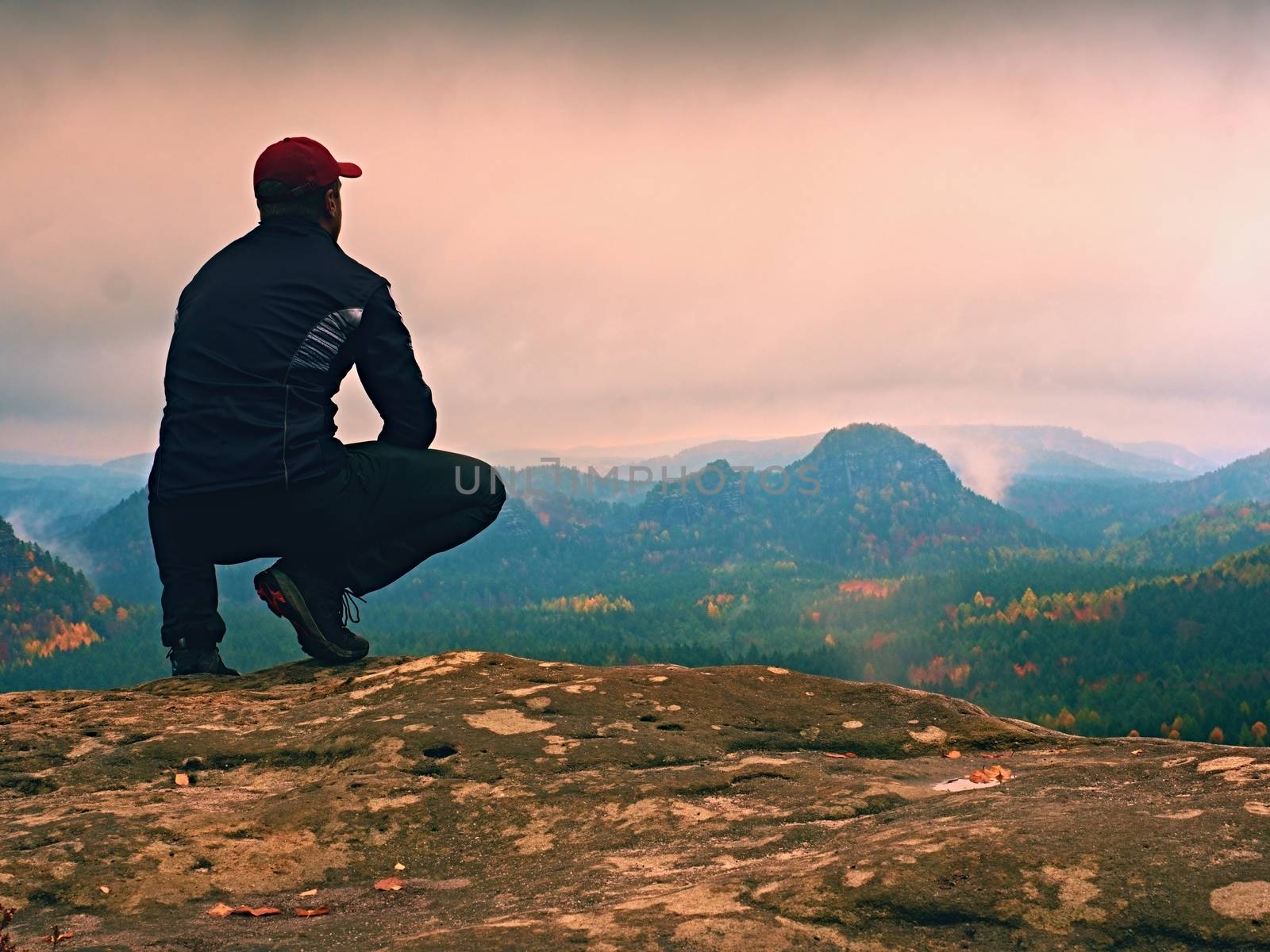 Tourist in black  sit on cliff's edge looking to misty hilly valley by rdonar2