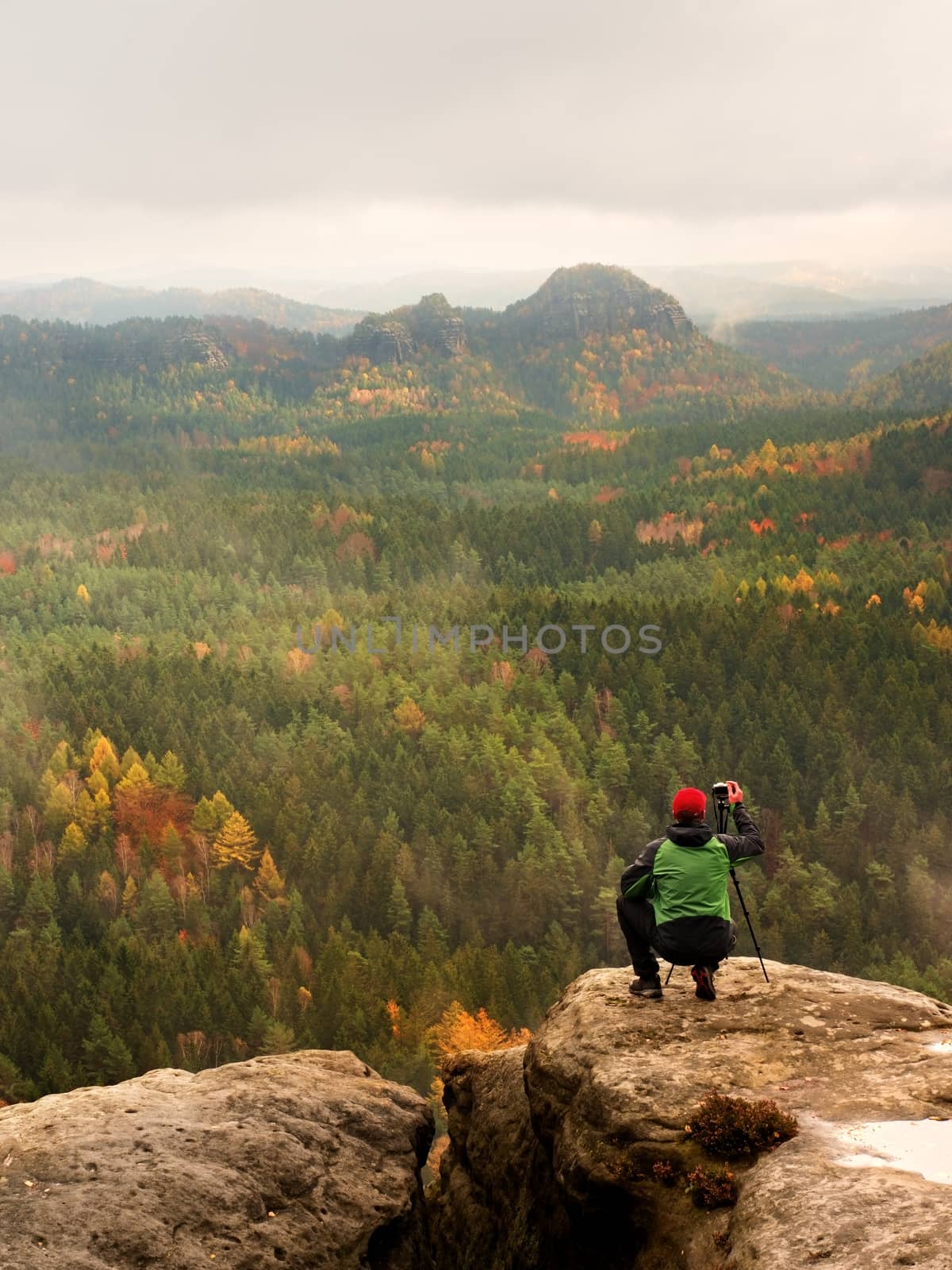 Photographer takes picture of spring nature from sharp rocks. Hiker in green jacket stay with camera on tripod  by rdonar2