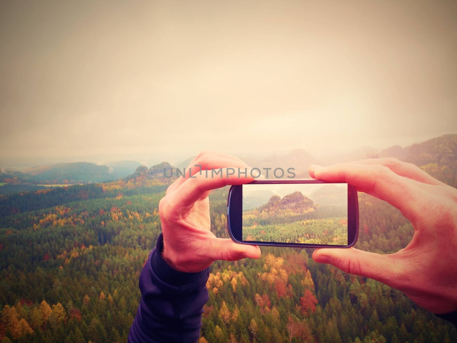 Man takes photos with phone on rock empire. Dreamy fogy mountains, spring orange pink misty sunrise in a beautiful valley of rocky mountains. by rdonar2