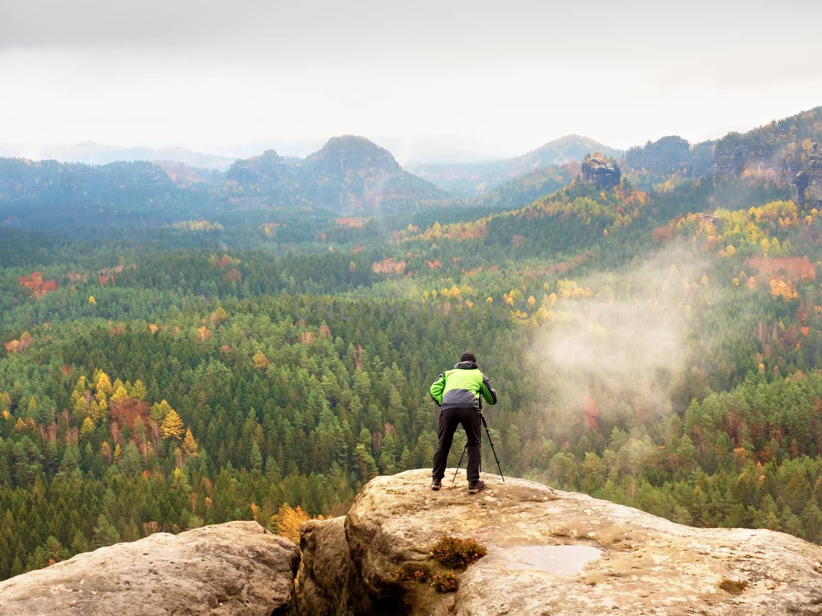 Hiker with camera on tripod takes picture from rocky summit. Alone photographer at edge photograph landscape by rdonar2