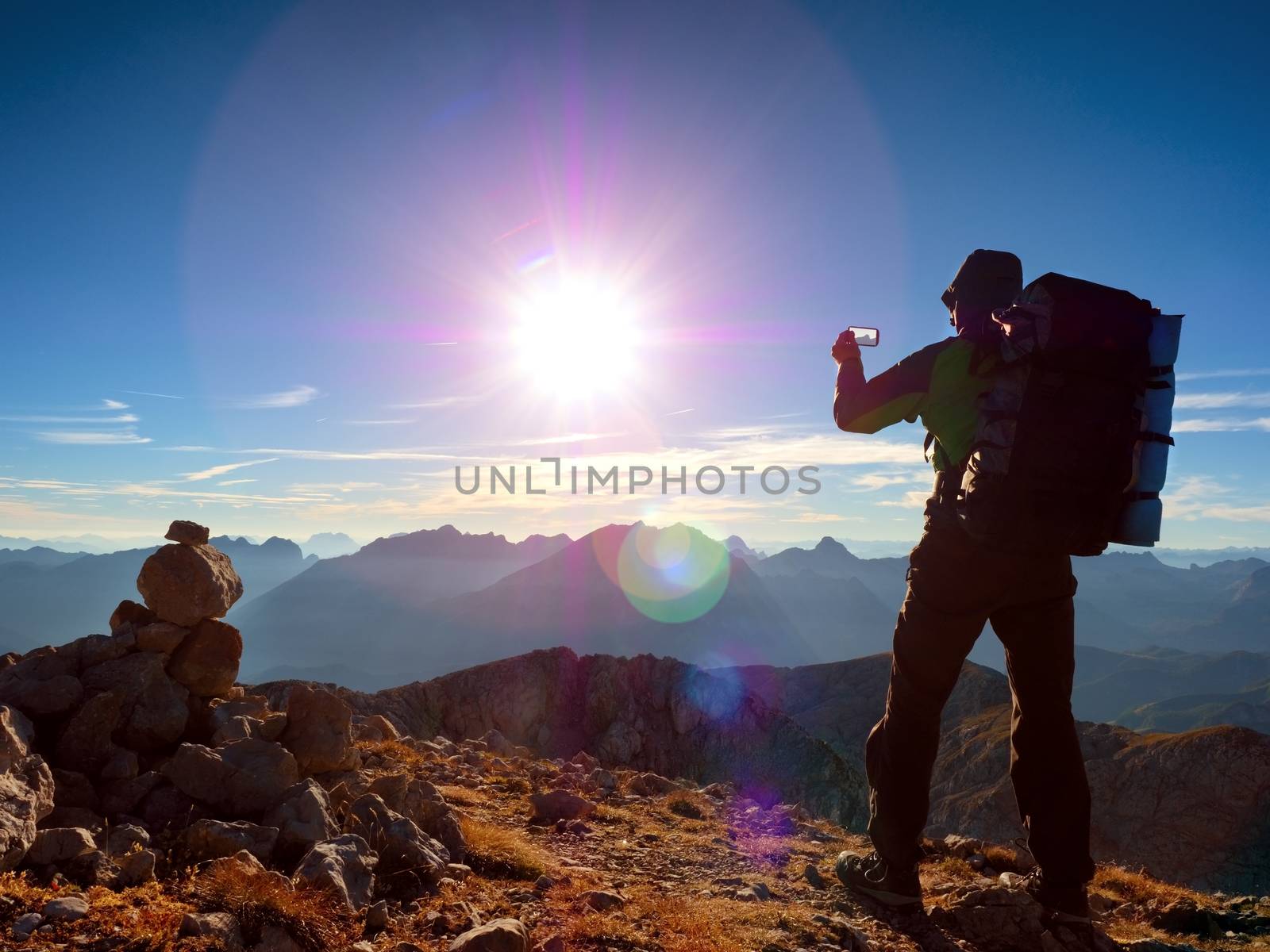 Lens flare light, strong defect. Tourist guide on Alps peak takes photo. Strong hiker with big backpack  Alpine mountain. Alone man on few days trek
