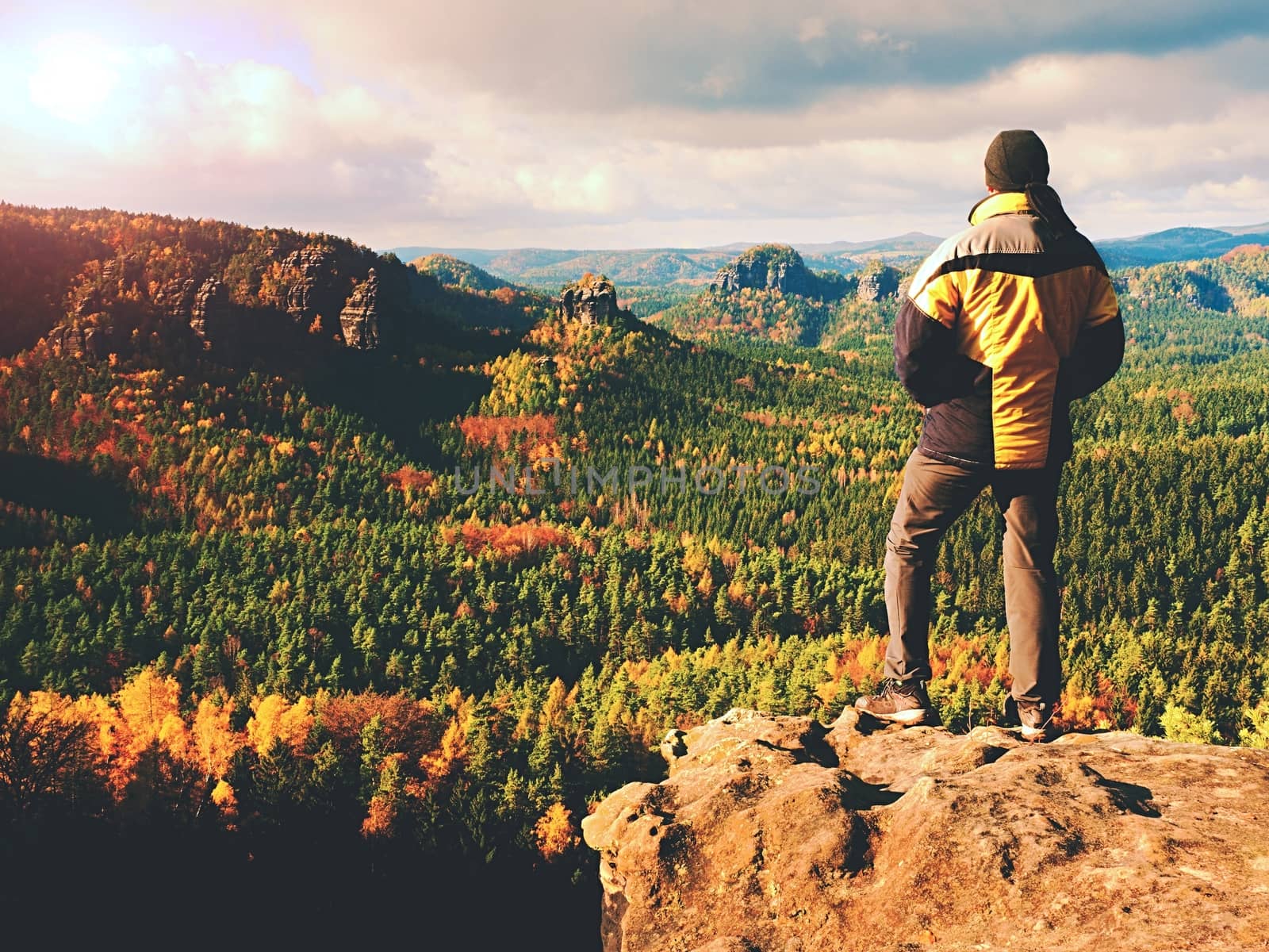 Man stay on sharp rock peak. Satisfy hiker enjoy view. Tall man on rocky cliff watching down to landscape. Vivid and strong vignetting effect.