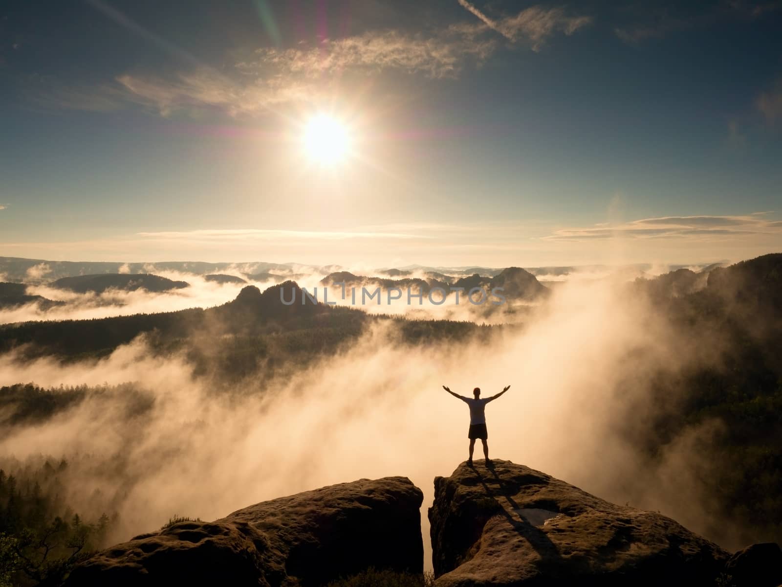 Happy man gesture of triumph with rams in air. Funny hiker on peak of sandstone rock in national park Saxony Switzerland watching to horizon