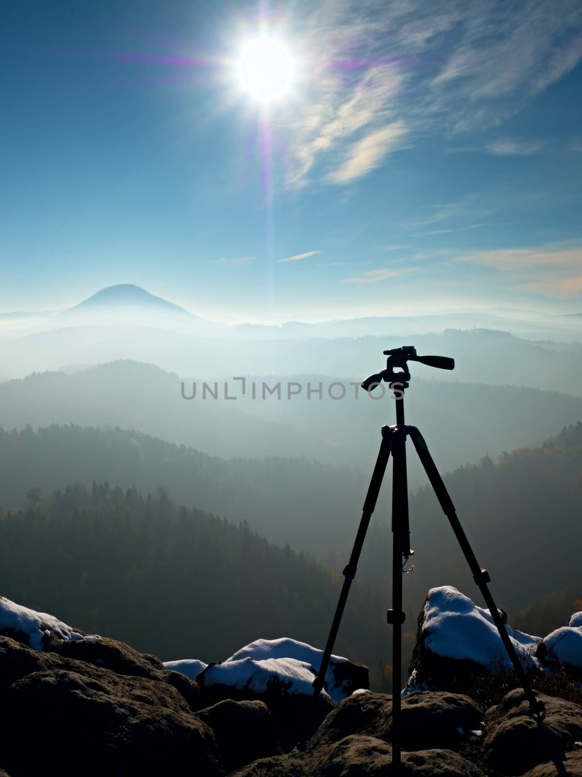 Professional  tripod without camera on snowy peak ready for photography. Snowy sandstone boulders,  first strong sun rays. 