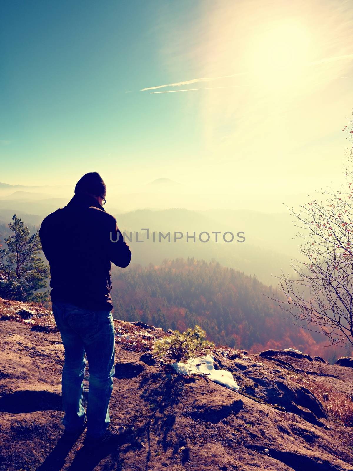 Tall  man is taking photo by mirror camera on neck. Snowy rocky peak of mountain. Professional photographer takes photos with mirror camera on peak of snowy rock. 