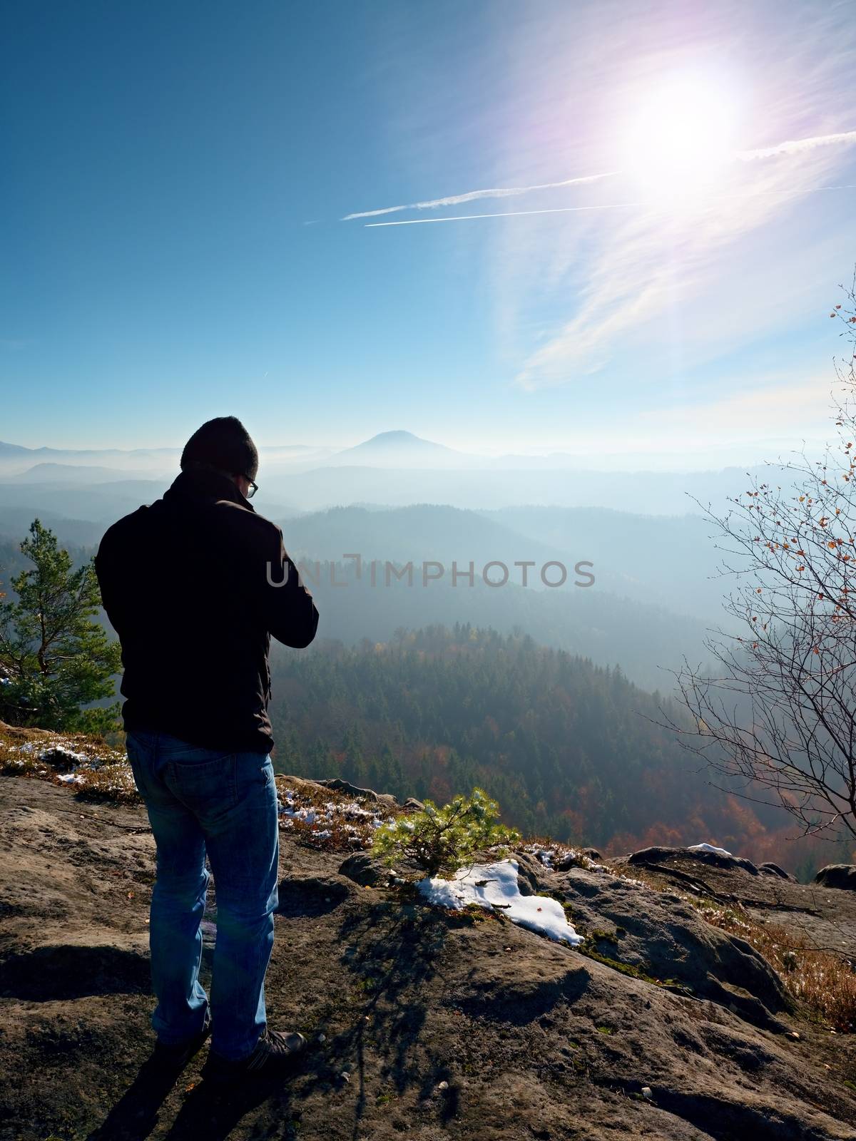 Tall  man is taking photo by mirror camera on neck. Snowy rocky peak of mountain. Professional photographer takes photos with mirror camera on peak of snowy rock. 