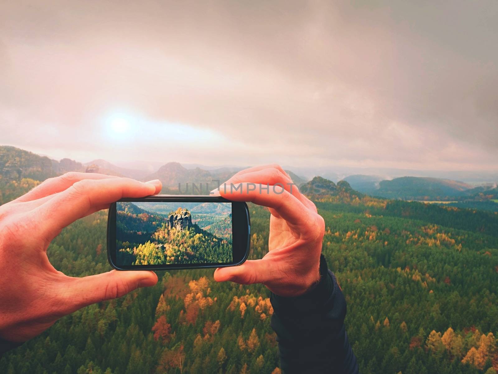 Man takes photos with phone on rock empire. Dreamy fogy mountains, spring orange pink misty sunrise in a beautiful valley of rocky mountains.