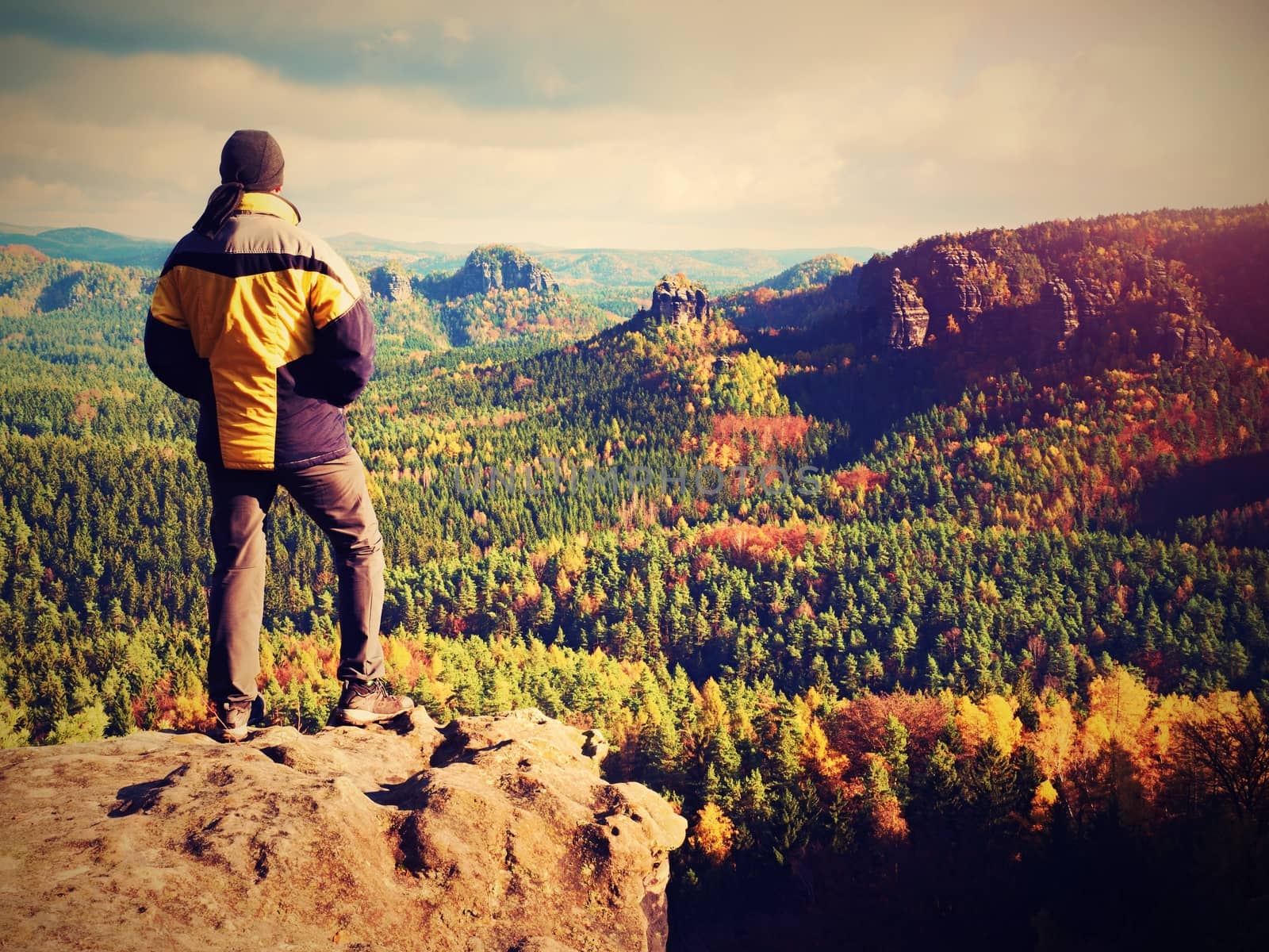 Man stay on sharp rock peak. Satisfy hiker enjoy view. Tall man on rocky cliff watching down to landscape. Vivid and strong vignetting effect.