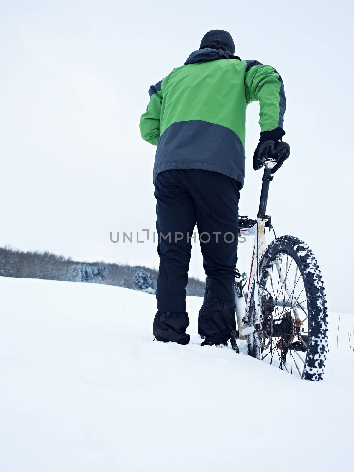 Man with mountain bike stay in powder snow. Lost path  in deep snowdrift. Rear wheel detail. Snow flakes melting on dark off road tyre.  Winter weather in the field.