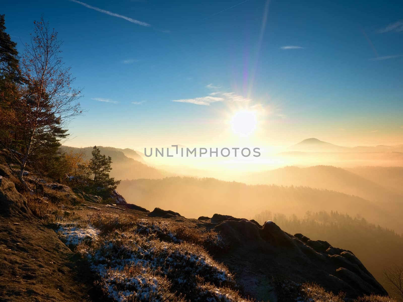 Cold golden spring daybreak. Snow on ground. Peaks of forests increased from the yellow and orange fog with sun rays. 
