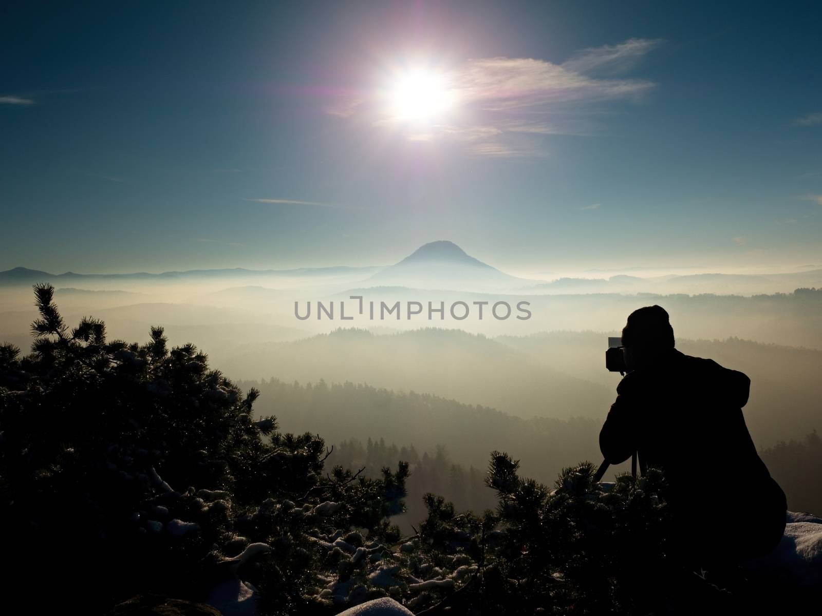 Tall  man is taking photo by mirror camera on neck. Snowy rocky peak of mountain. Professional photographer takes photos with mirror camera on peak of snowy rock. 