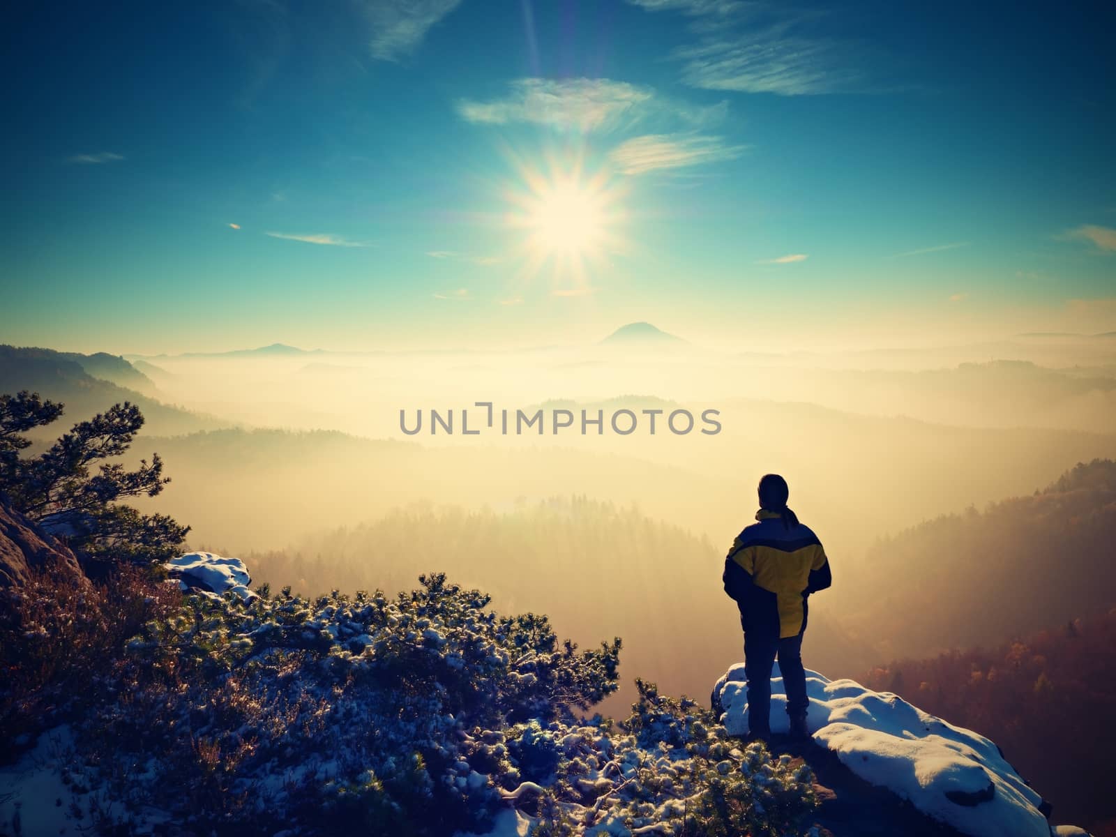 Tall hiker in black on rocky peak watch the world . Heavy orange mist bellow in valley. Wonderful breathtaking daybreak in mountains.