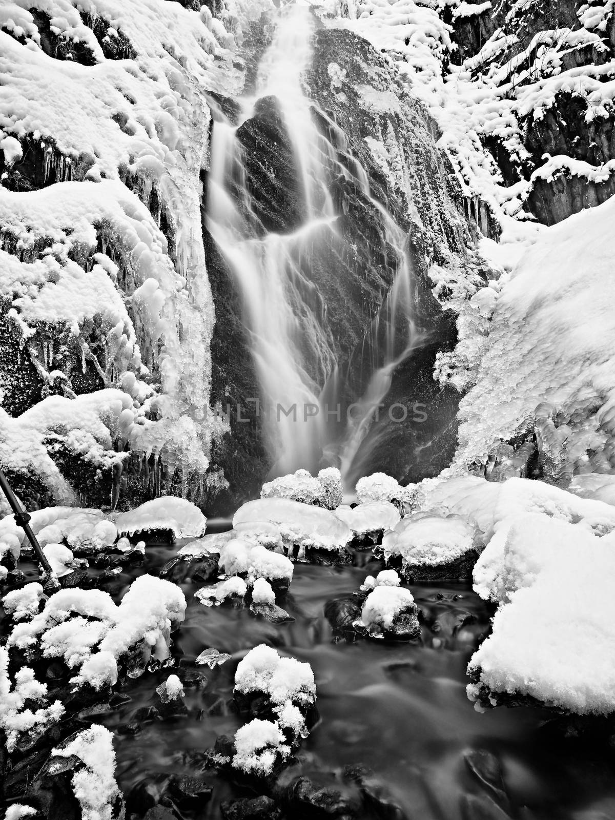 Frozen waterfall. Winter creek, icy stones and branches fallen into chilly water of mountain stream