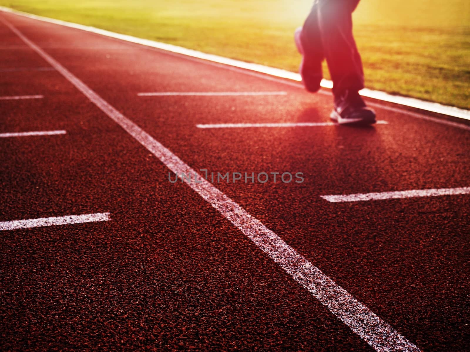 Sportsman on red running stadium racetrack. Adult man in evening training at sunset. Sport and healthy lifestyle concept and jogging civic training workout