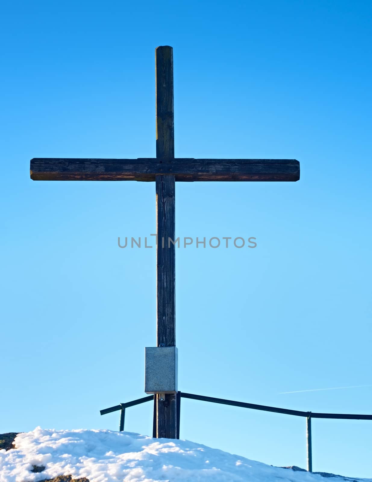 Sharp summit  with modest cross raised  on mountain peak. Winter daybreak Sun in sky. Wooden unpretentious crucifix in memory of victims of mountains. Vivid photo.