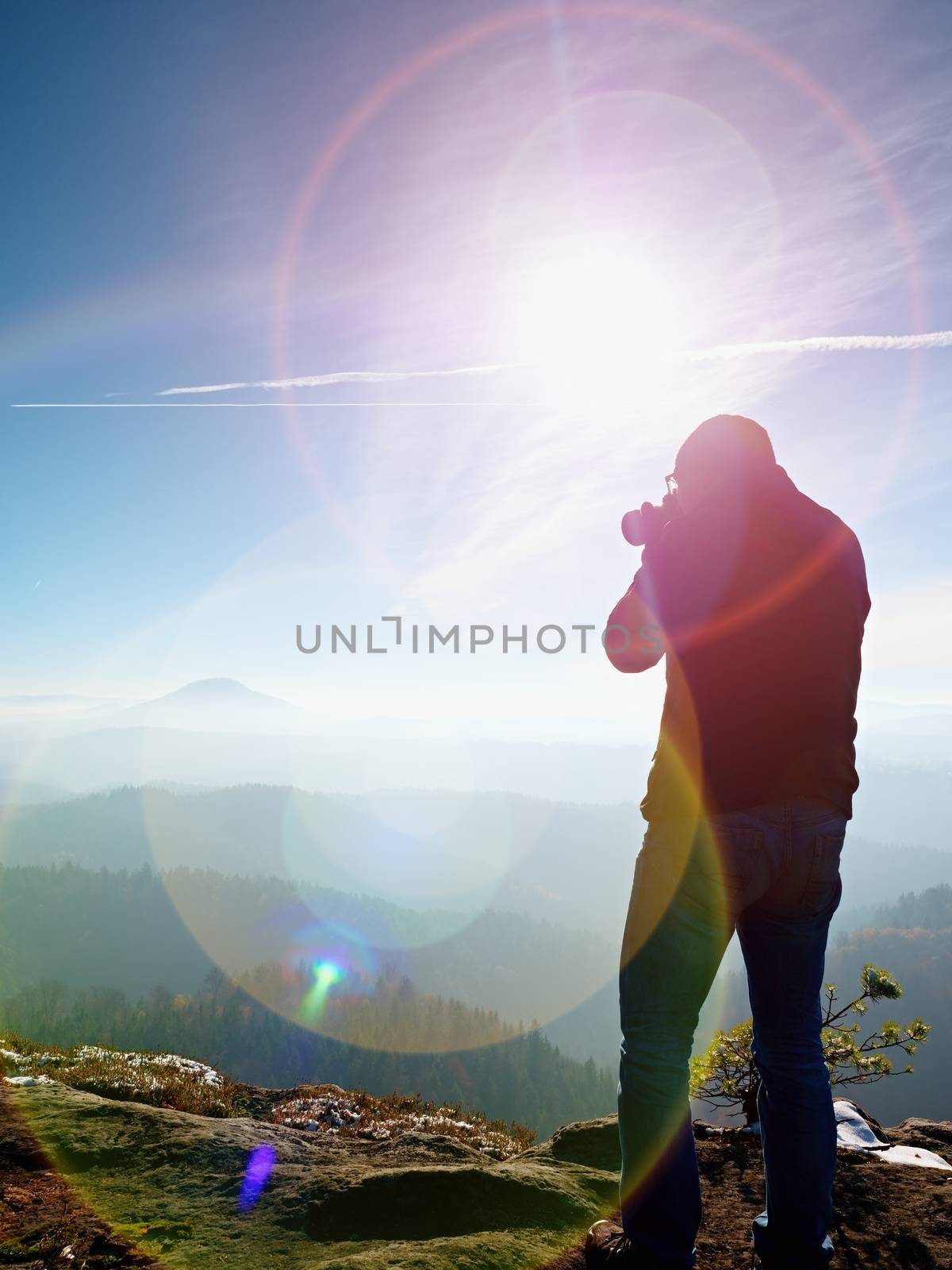 Tall  man is taking photo by mirror camera on neck. Snowy rocky peak of mountain. Professional photographer takes photos with mirror camera on peak of snowy rock. 