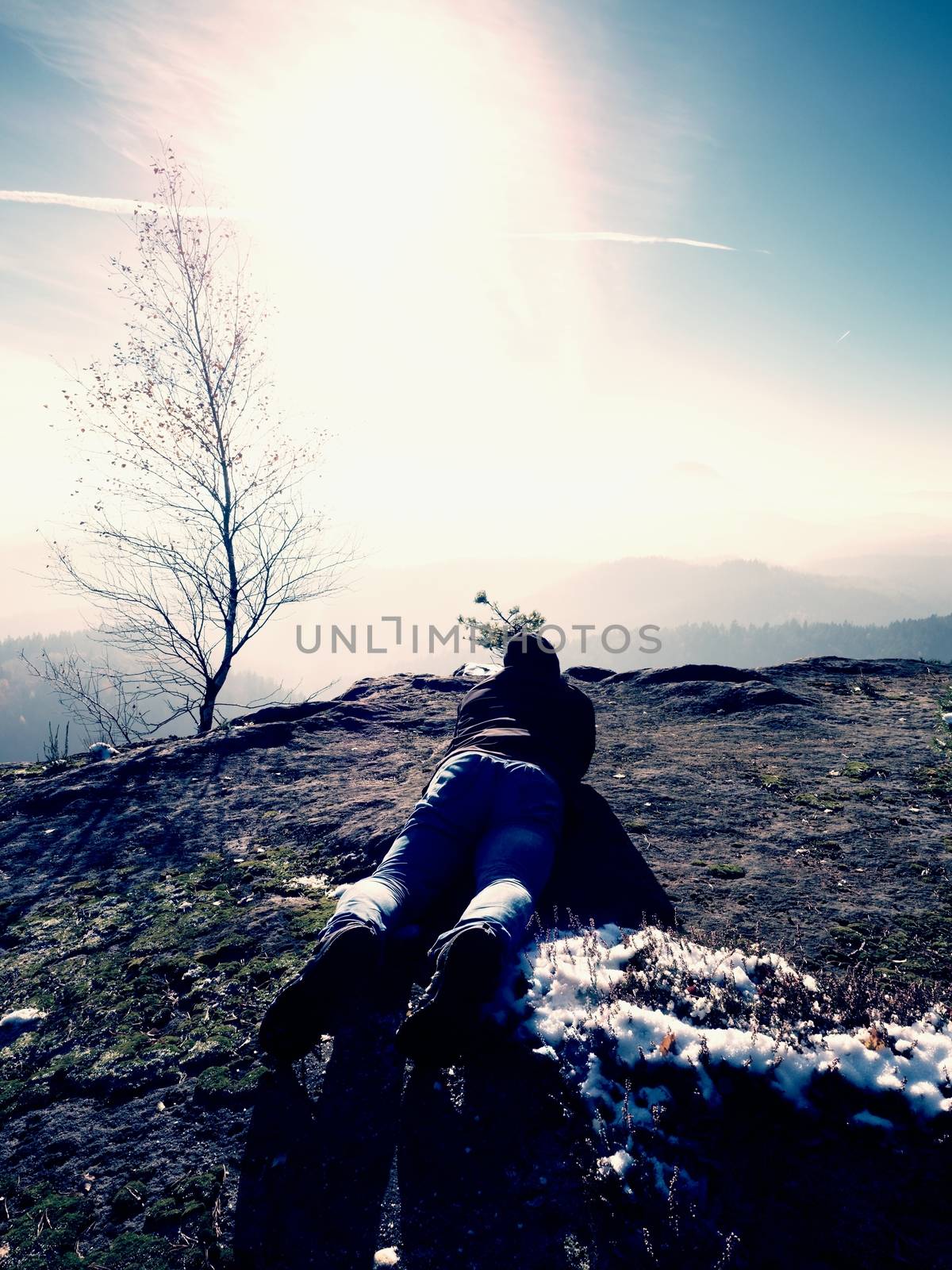 Man lay down and  taking photo by mirror camera on neck. Snowy rocky peak of mountain. Professional photographer takes photos with mirror camera on peak of snowy rock. 