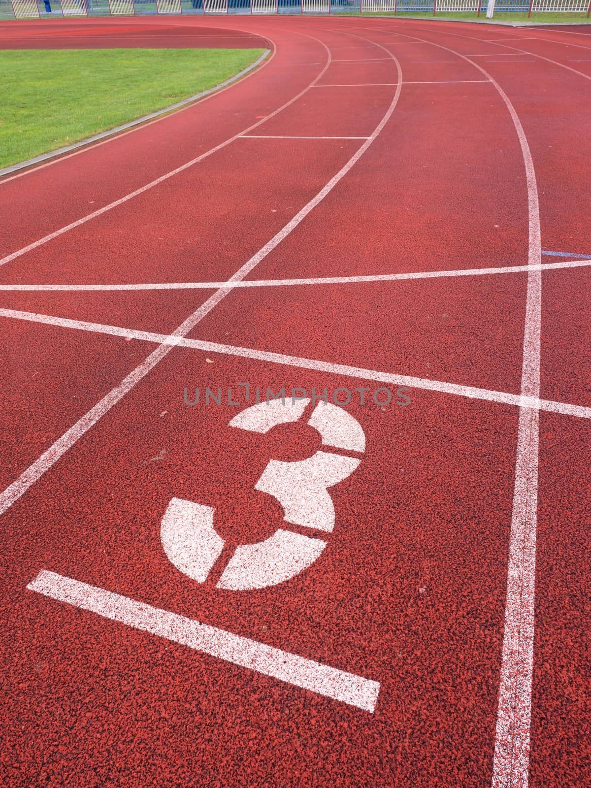 Number three. Big white track number on red rubber racetrack. Gentle textured racetracks in small outdoor stadium.