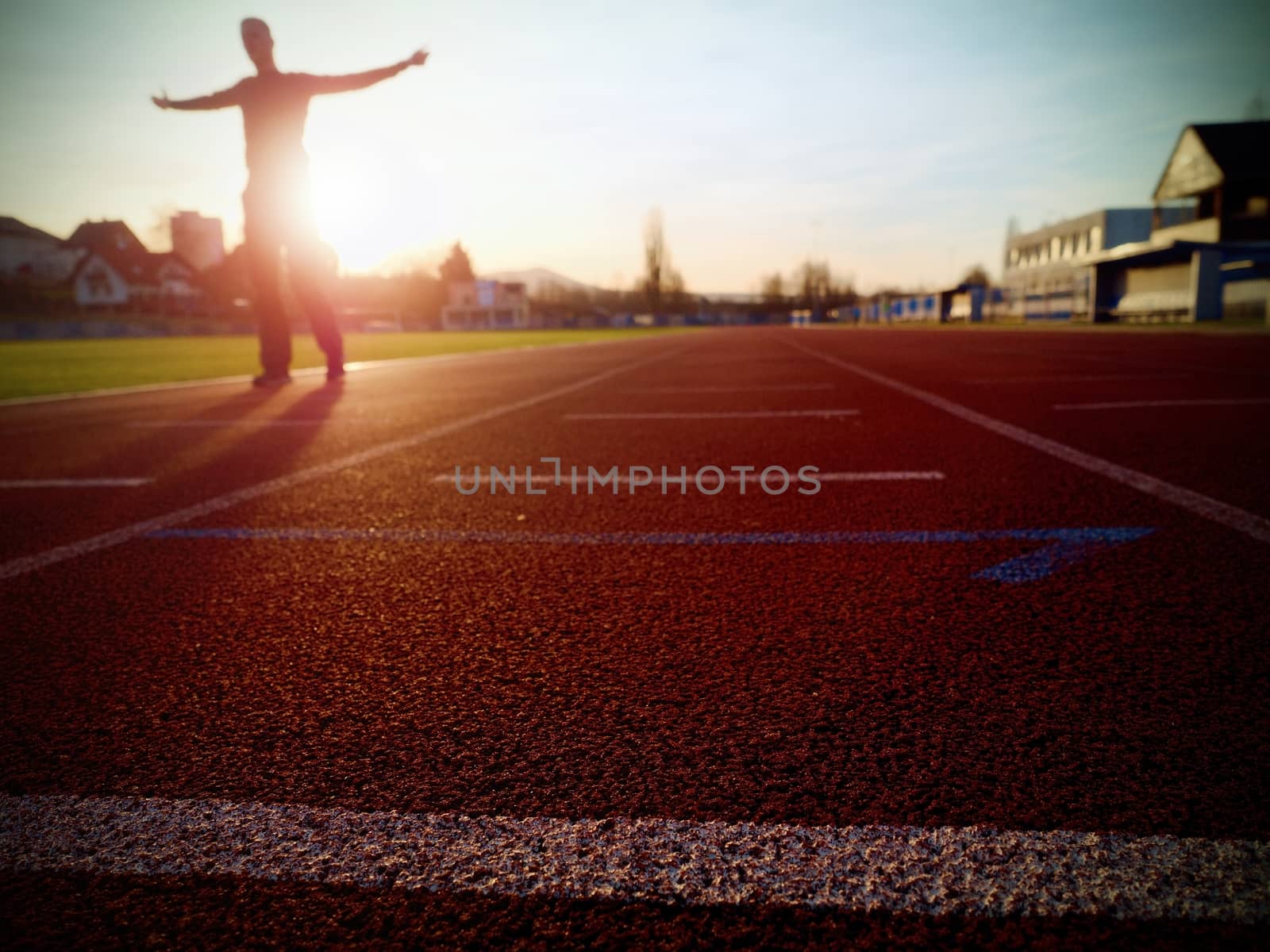 Tall man running on red running racetrack on the stadium. Sportsman in training clothes at amazing sunset. Sport and healthy lifestyle concept and jogging civic training workout